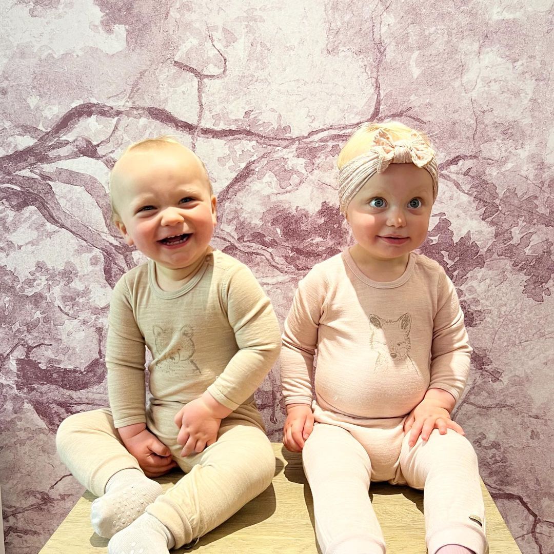 Deux jeunes enfants souriants, vêtus de pyjamas assortis à imprimé de renard, sont assis contre un mur à motifs.