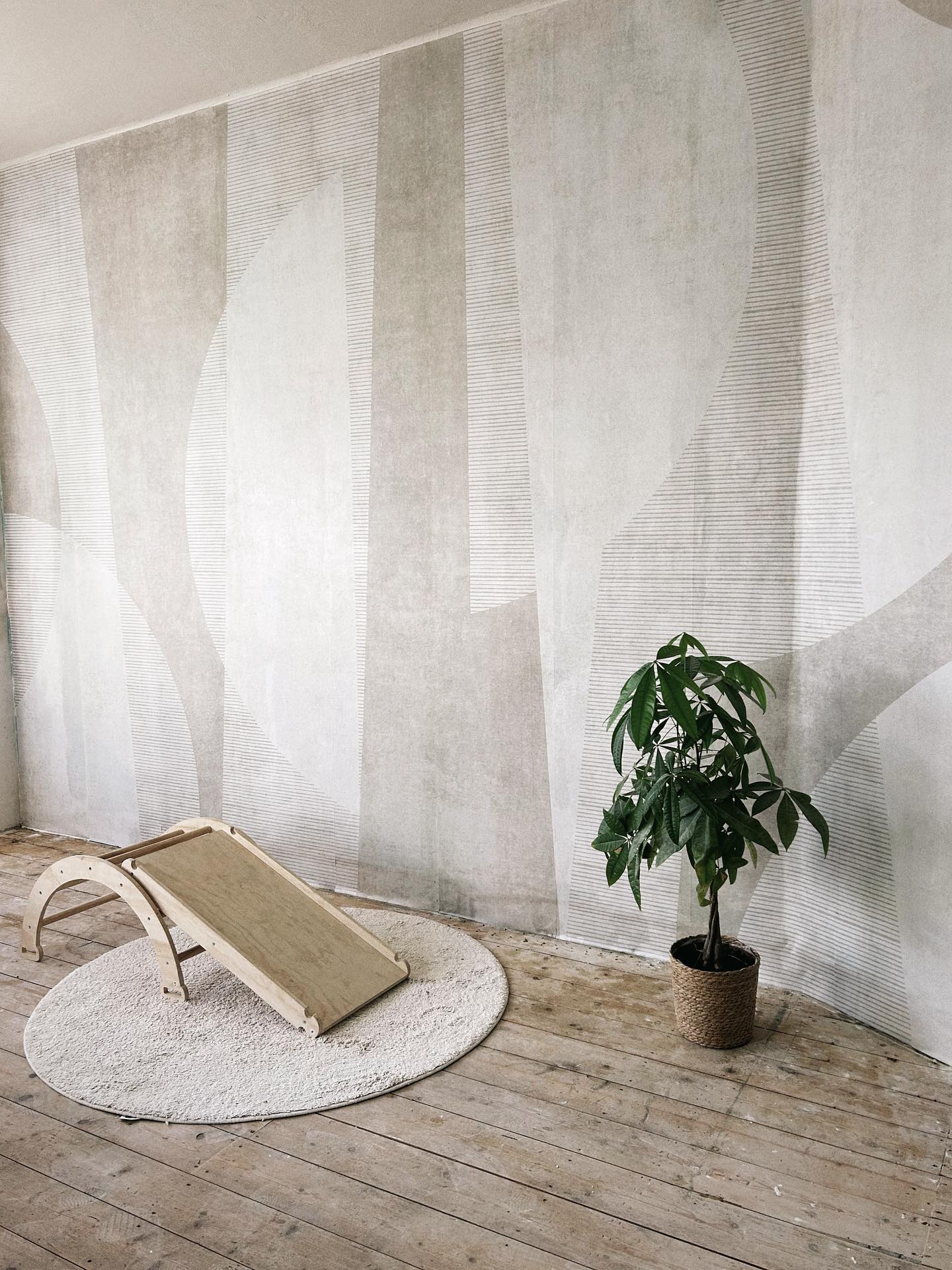 Minimalist room with geometric wallpaper, wooden slide on a round rug, and potted plant.