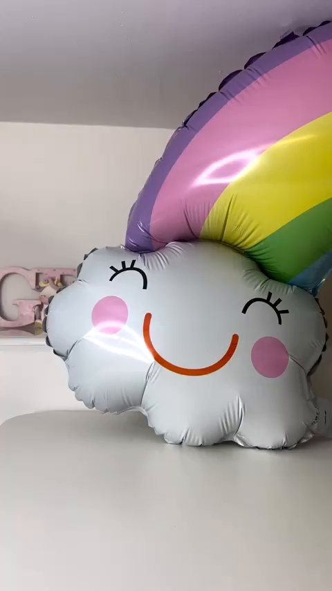 Smiling cloud balloon with rainbow on a white table.