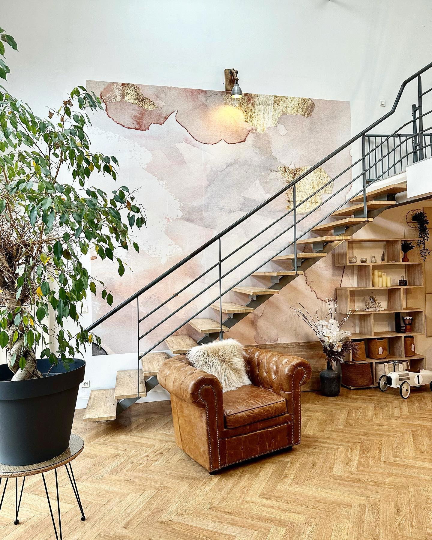 Living room with brown leather armchair, wood stairs, and abstract wall art.