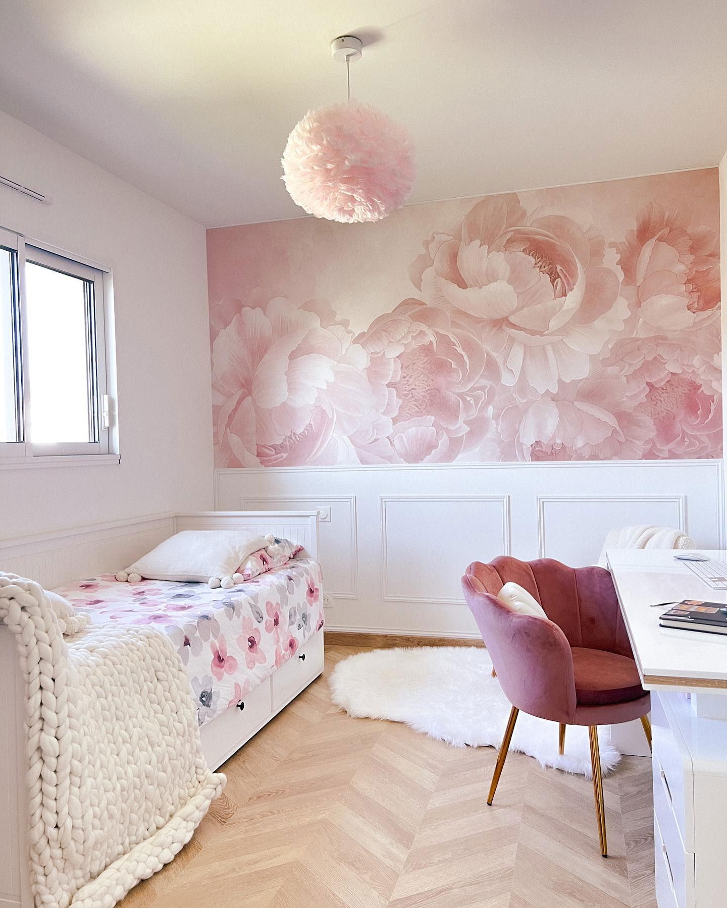Camera da letto con carta da parati floreale, letto bianco con biancheria da letto floreale e sedia in velluto rosa.