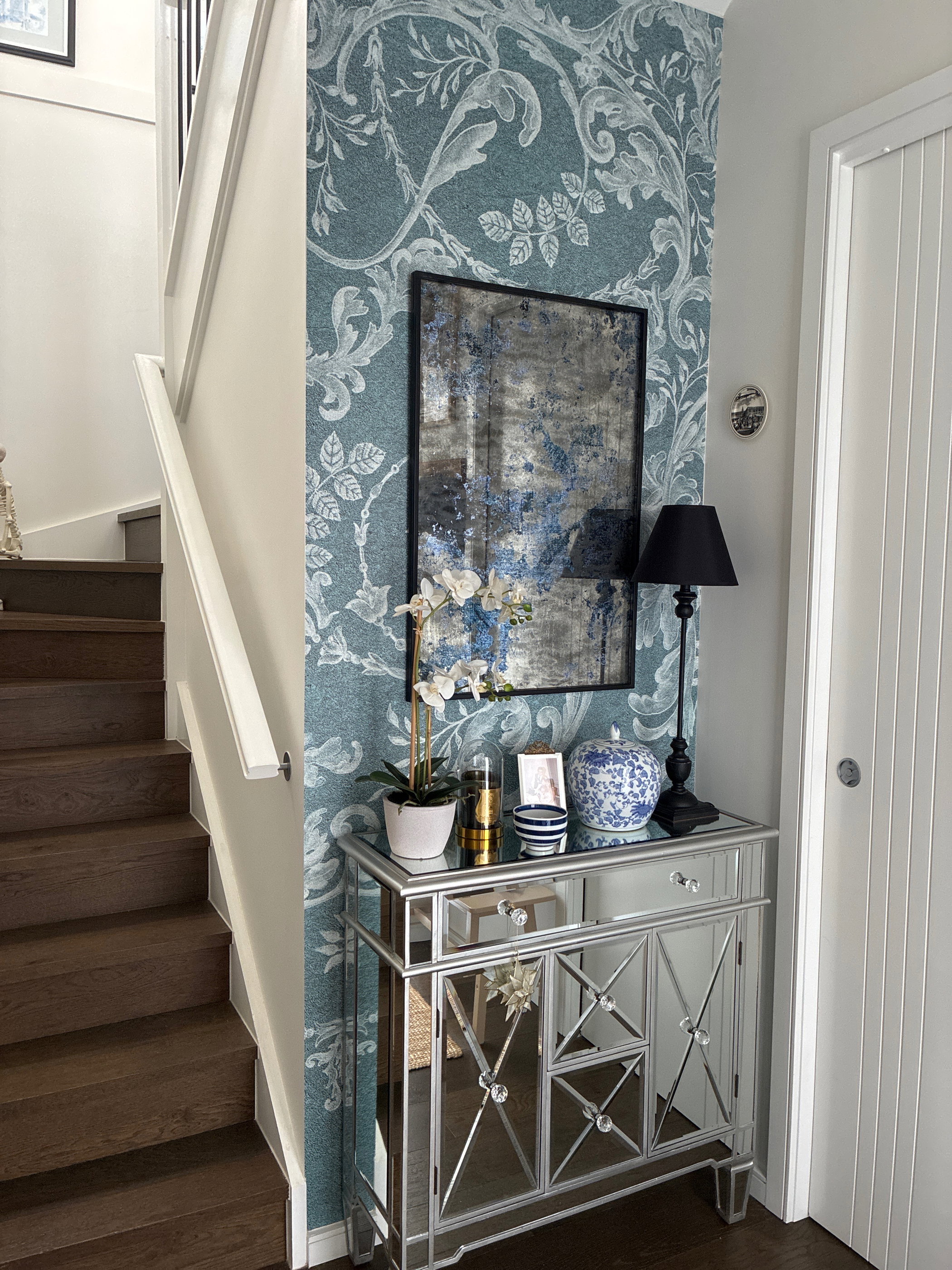 Hallway with mirrored cabinet, abstract art, and floral wallpaper.
