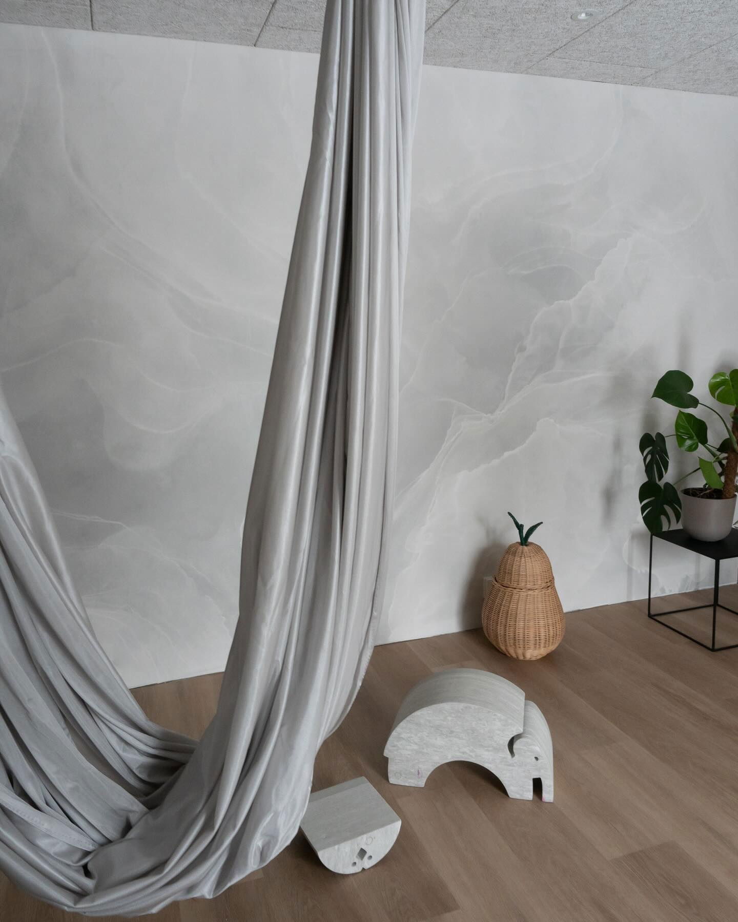 Intérieur avec hamac de yoga aérien gris, sculpture d'éléphant en pierre et panier en forme de poire.