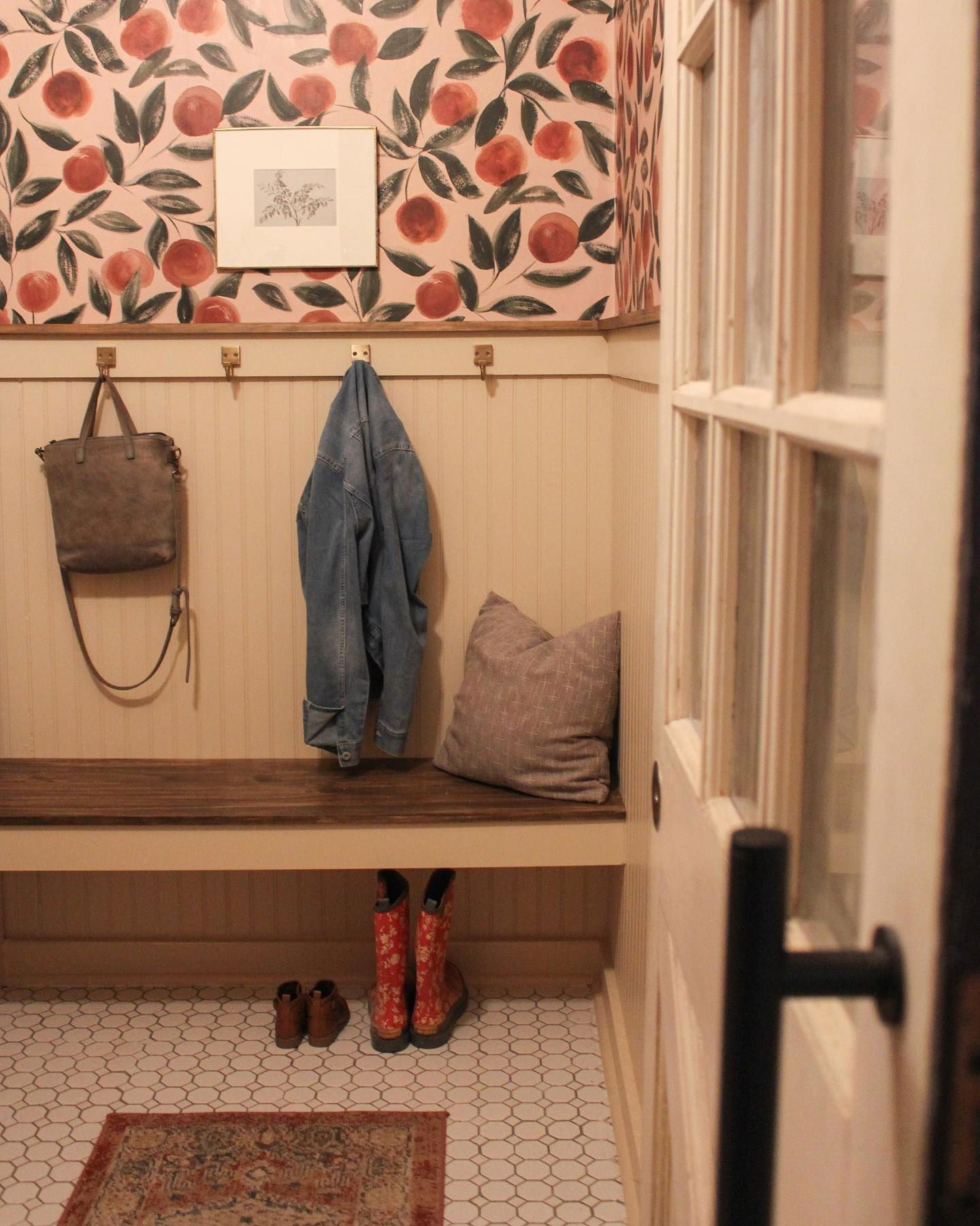 Mudroom with peach wallpaper, bench, hooks with bag and jacket, and shoes underneath.