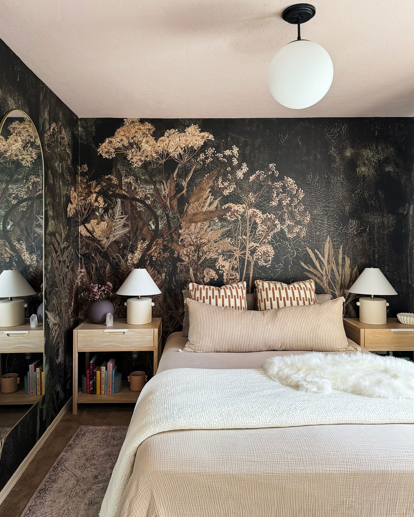 Schlafzimmer mit floraler Tapete, neutraler Bettwäsche und hellen Holz Nachttischen.