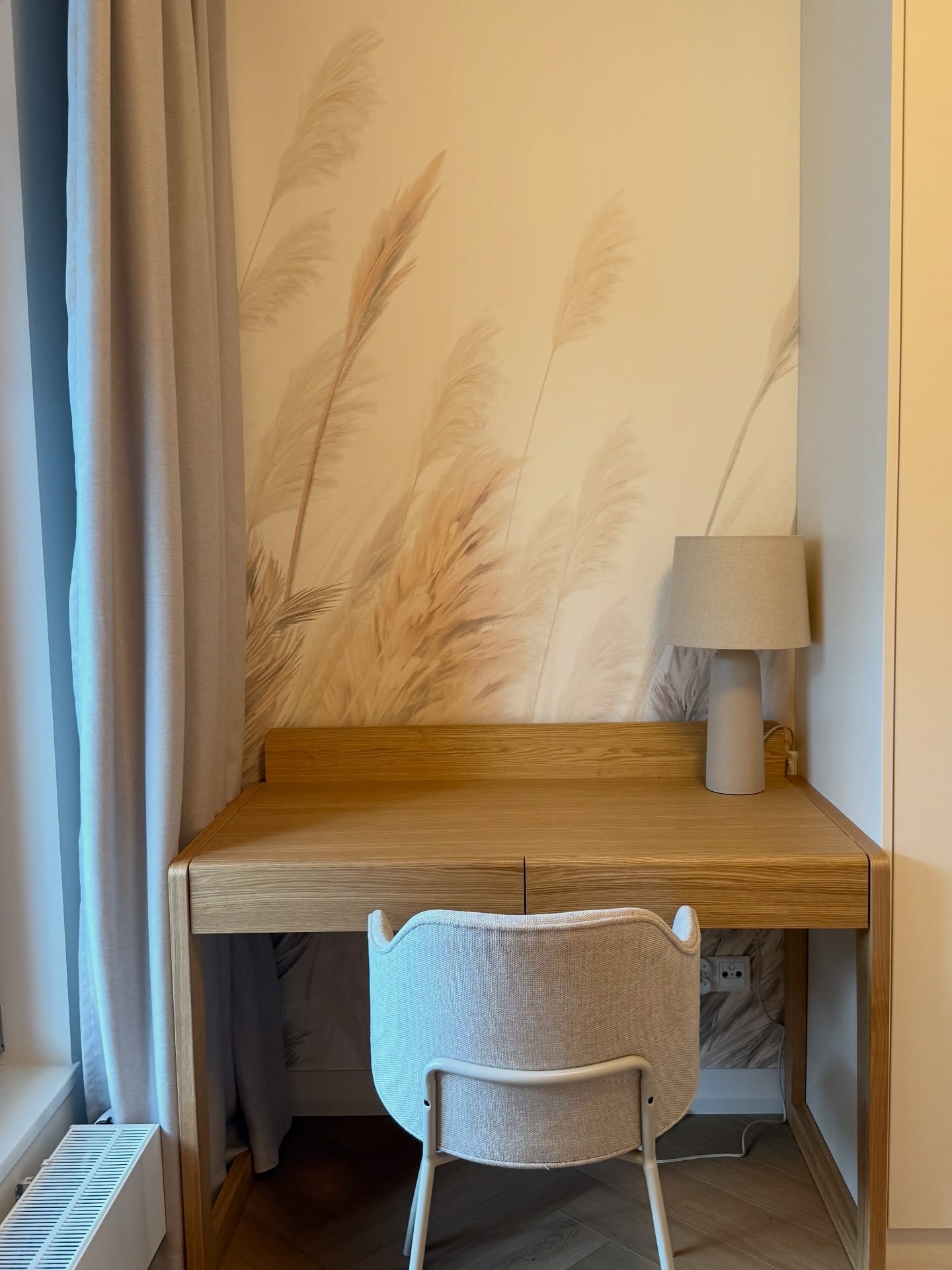 Desk area with light wood desk, gray chair, and lamp. Wall has a wheat stalk design.