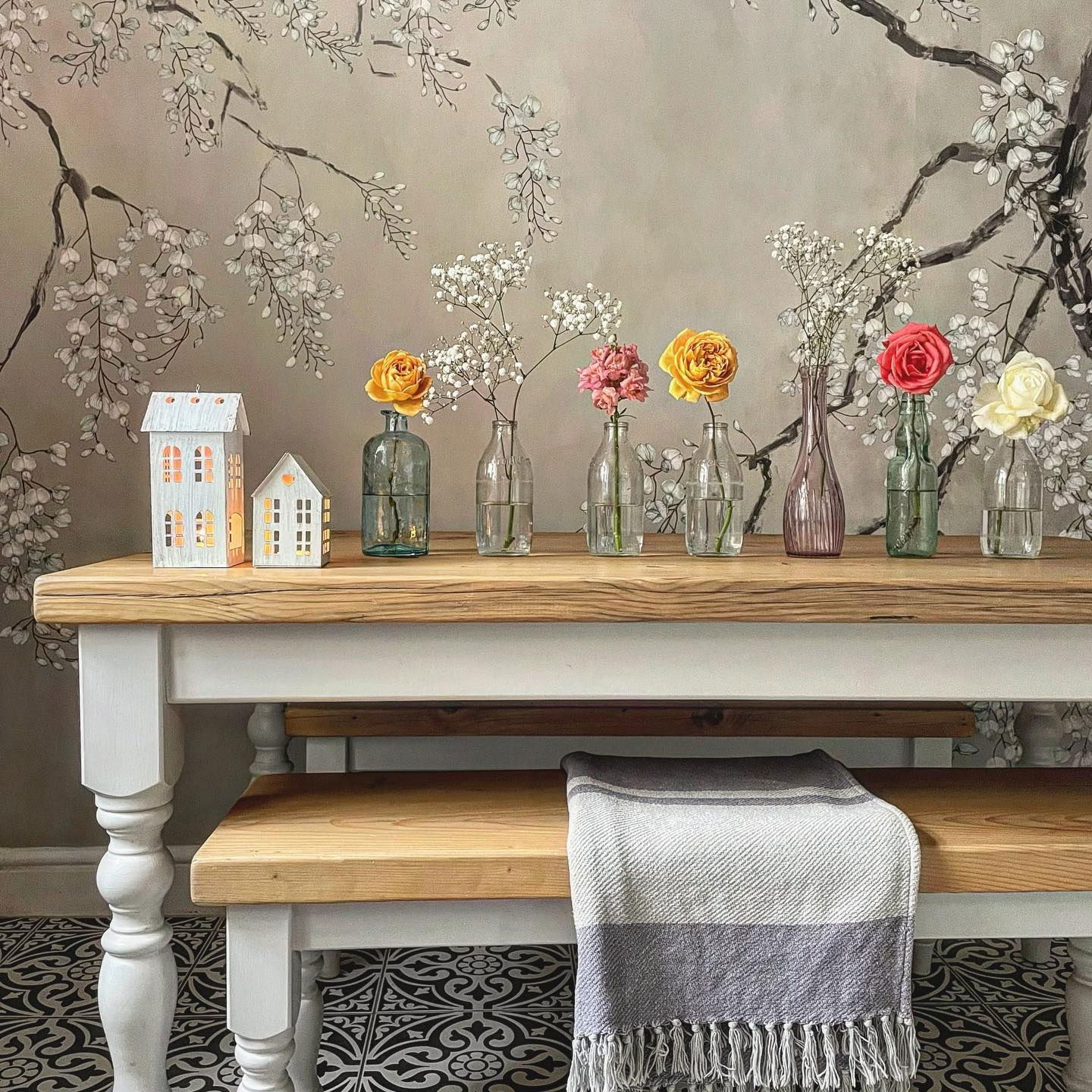 Dining table with flowers in vases, decorative houses, and a gray striped throw blanket.