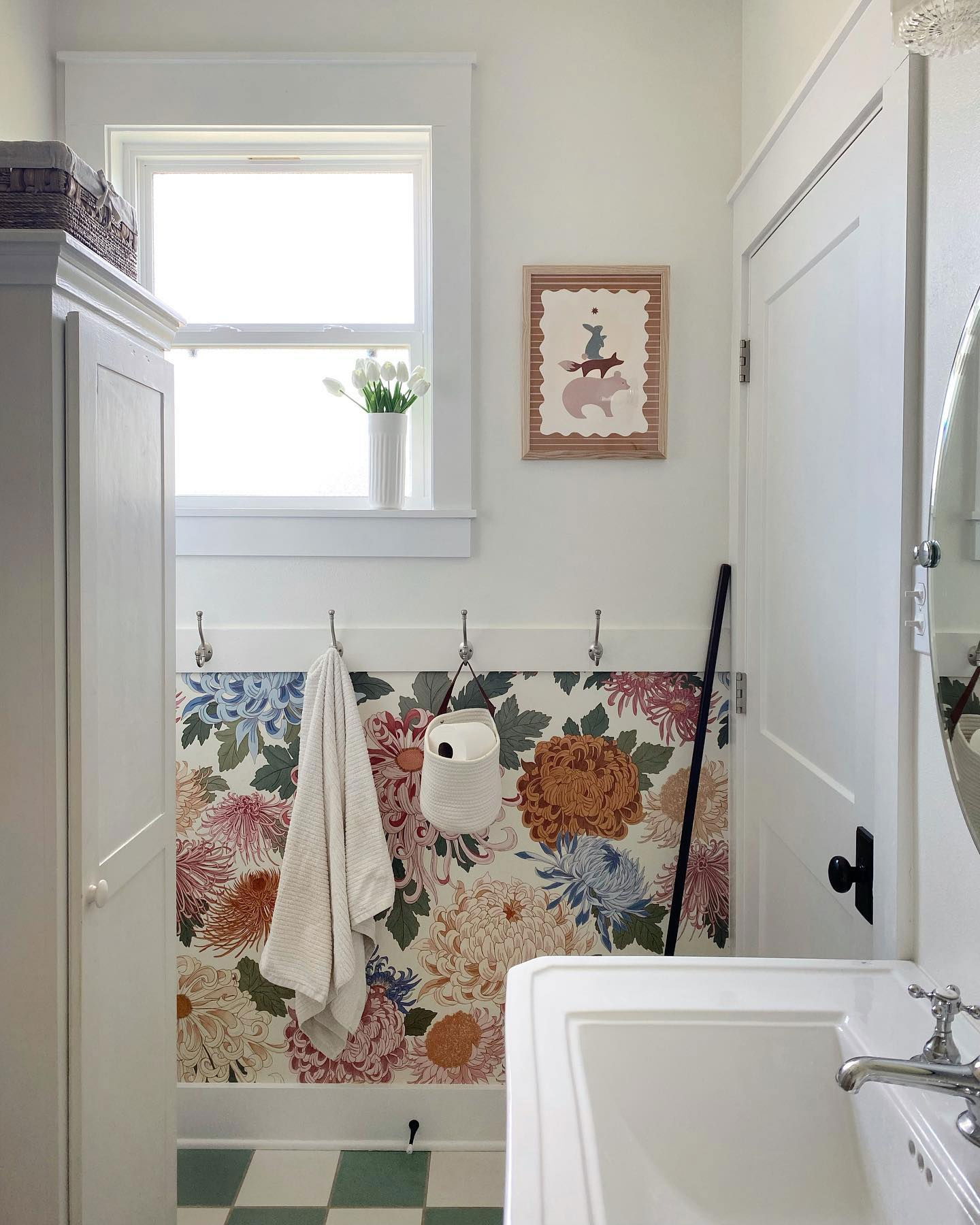 Bathroom with floral wallpaper, white vanity, and green and white checkered floor. A framed animal print hangs on the wall.