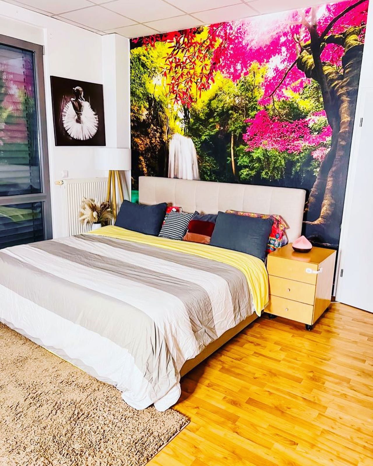Schlafzimmer mit gestreifter Bettwäsche, farbenfrohem Wandbild und Ballerina-Kunst.