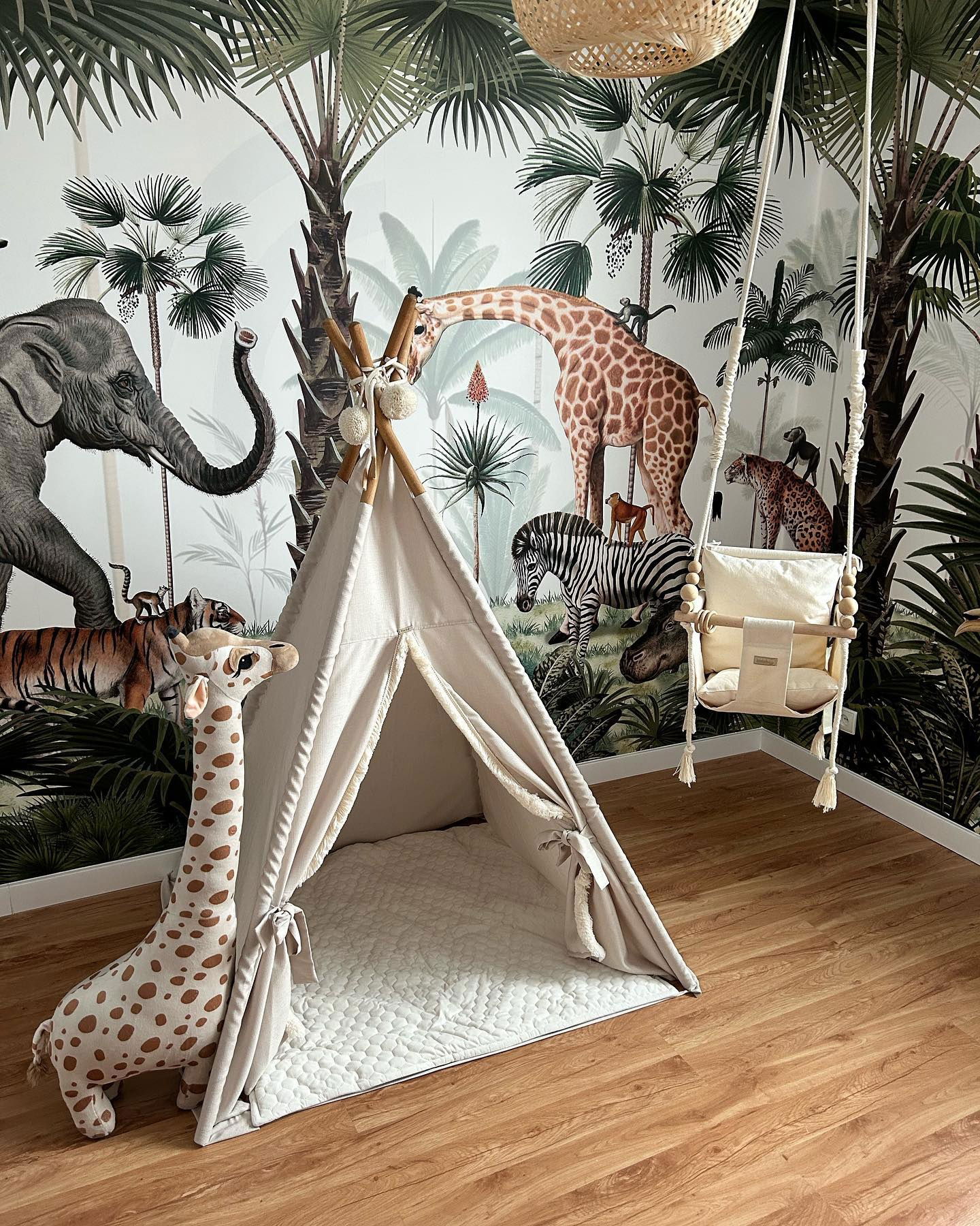 Barnerom med jungeltapet, beige tipi, utstoppet giraff og hengende huskesete.