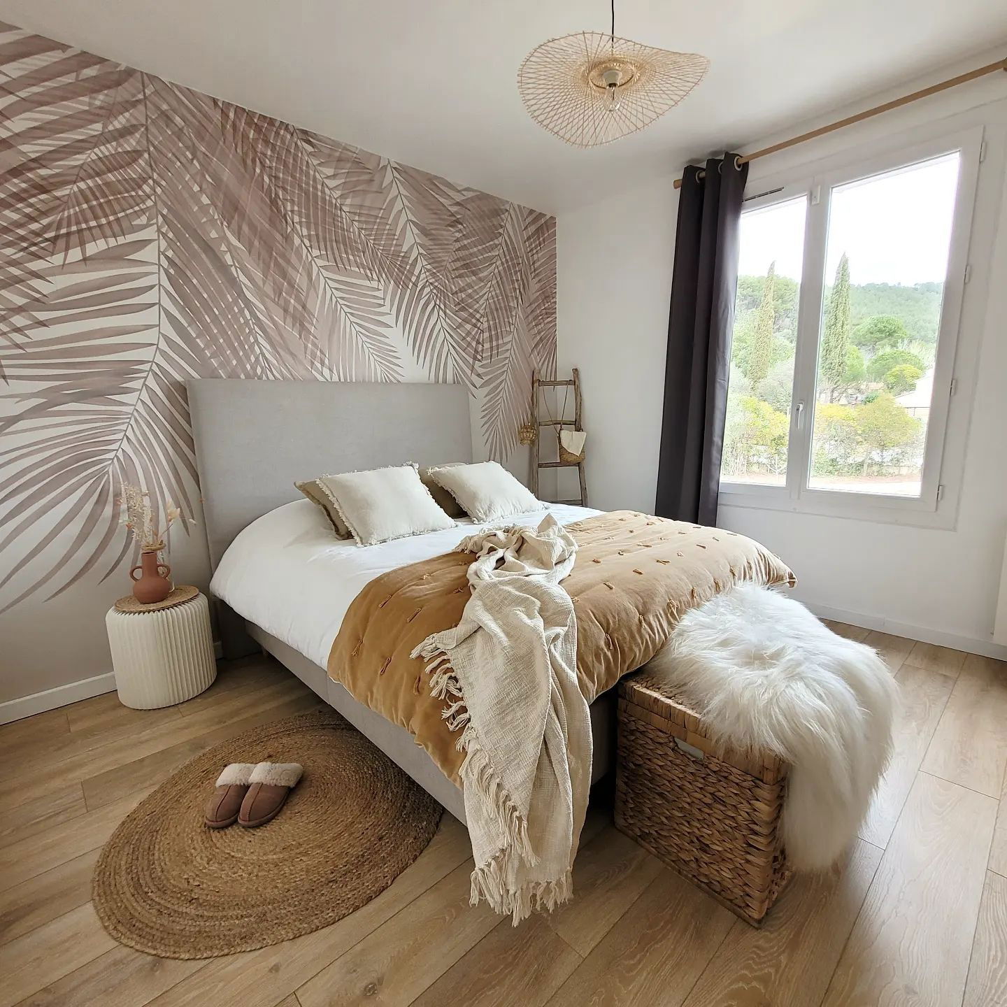 Bedroom with palm leaf wallpaper, neutral bedding, and woven accents. Window view.