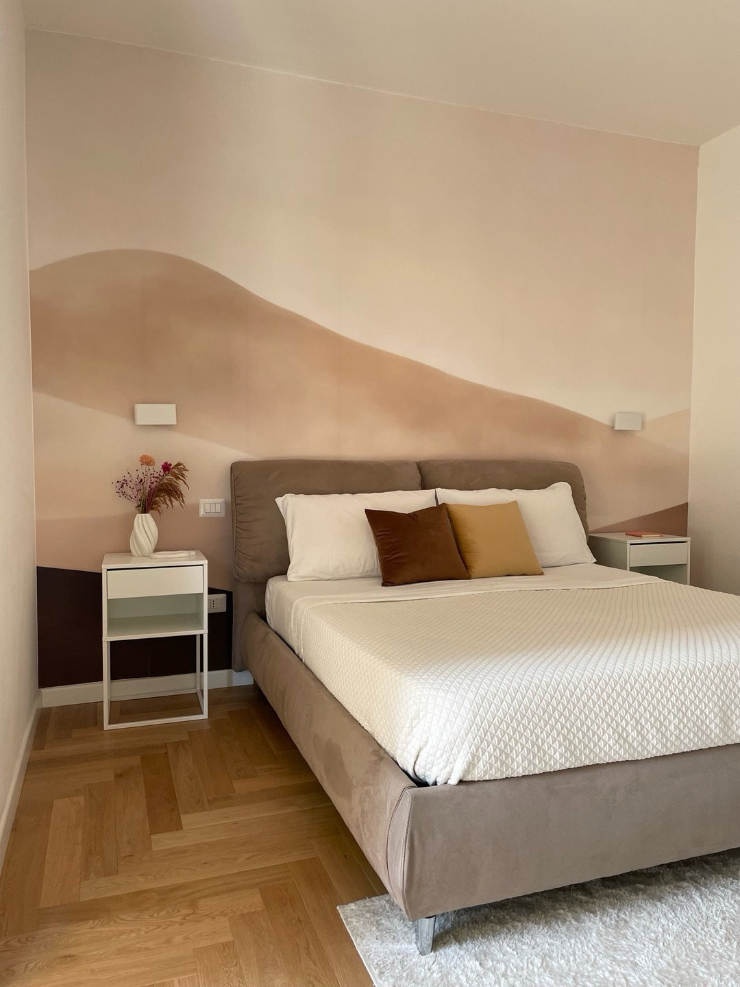 Bedroom with a bed, desert mural wallpaper, and bedside table with flowers.