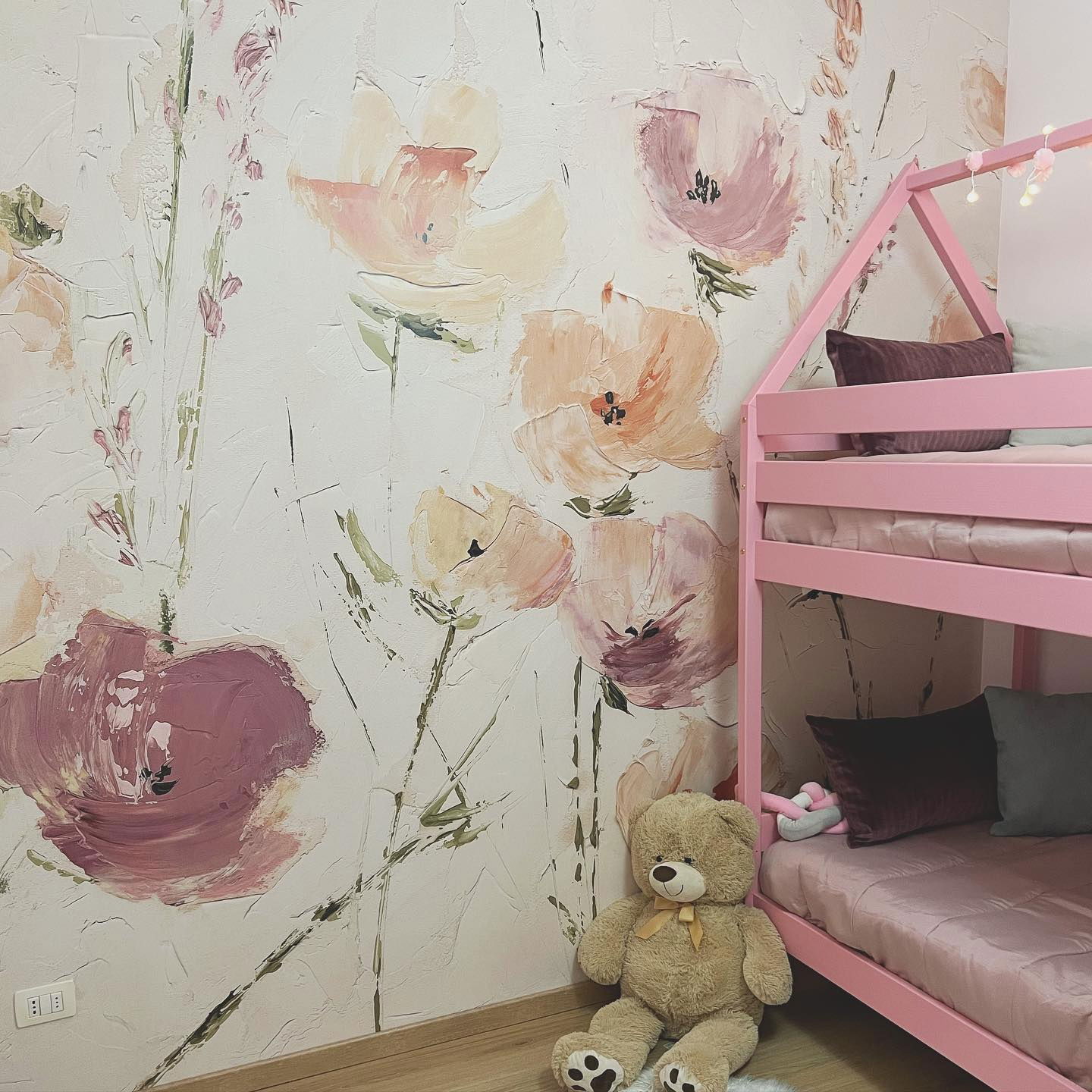 Kinderzimmer mit rosa Etagenbett, Blumentapete und Teddybär.