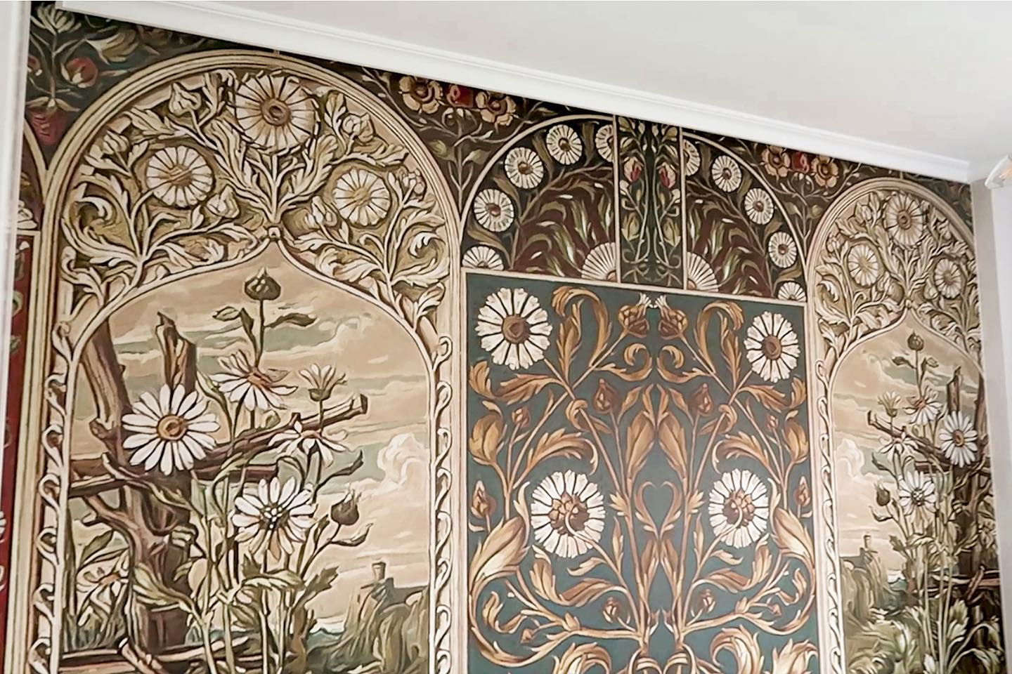 Pared con papel tapiz floral en paneles arqueados, en tonos de marrón, verde y blanco.