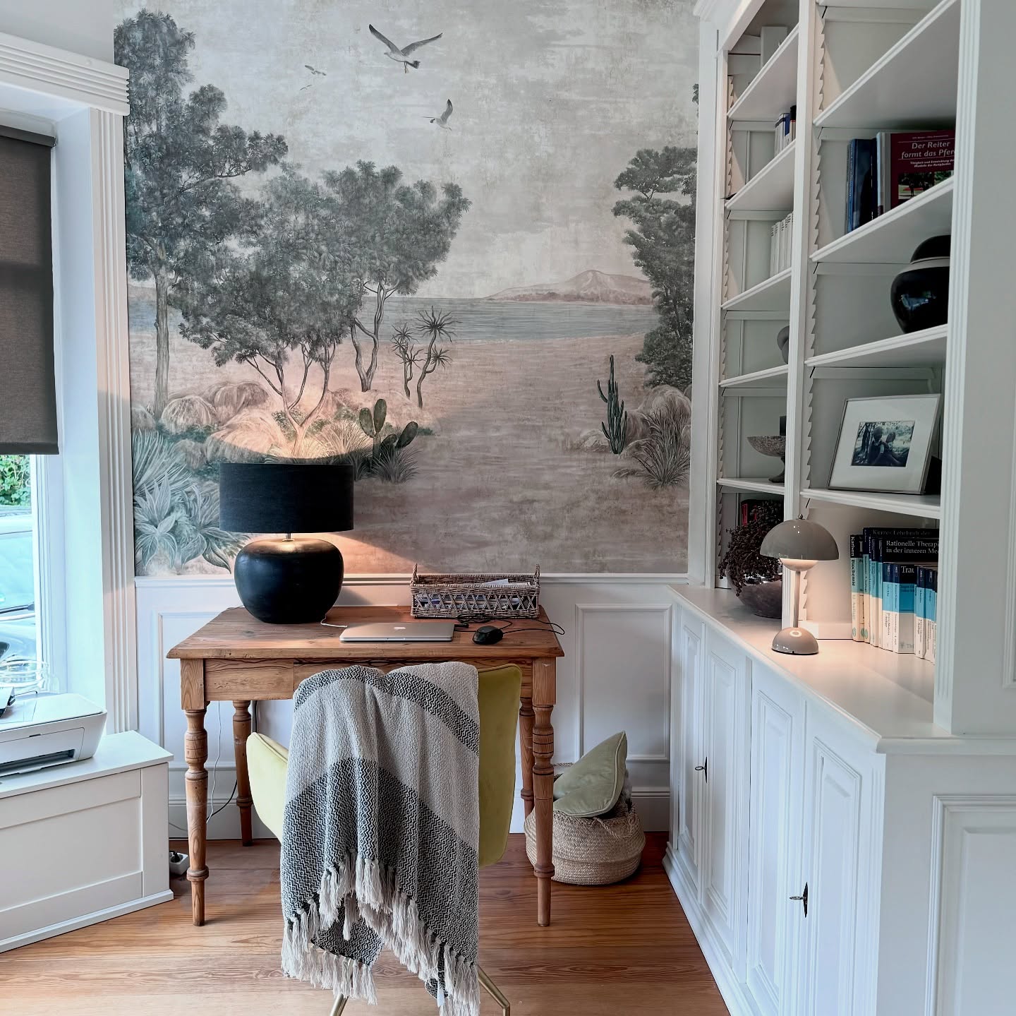 Home office with desert mural, wooden desk, and white built-in bookcase.