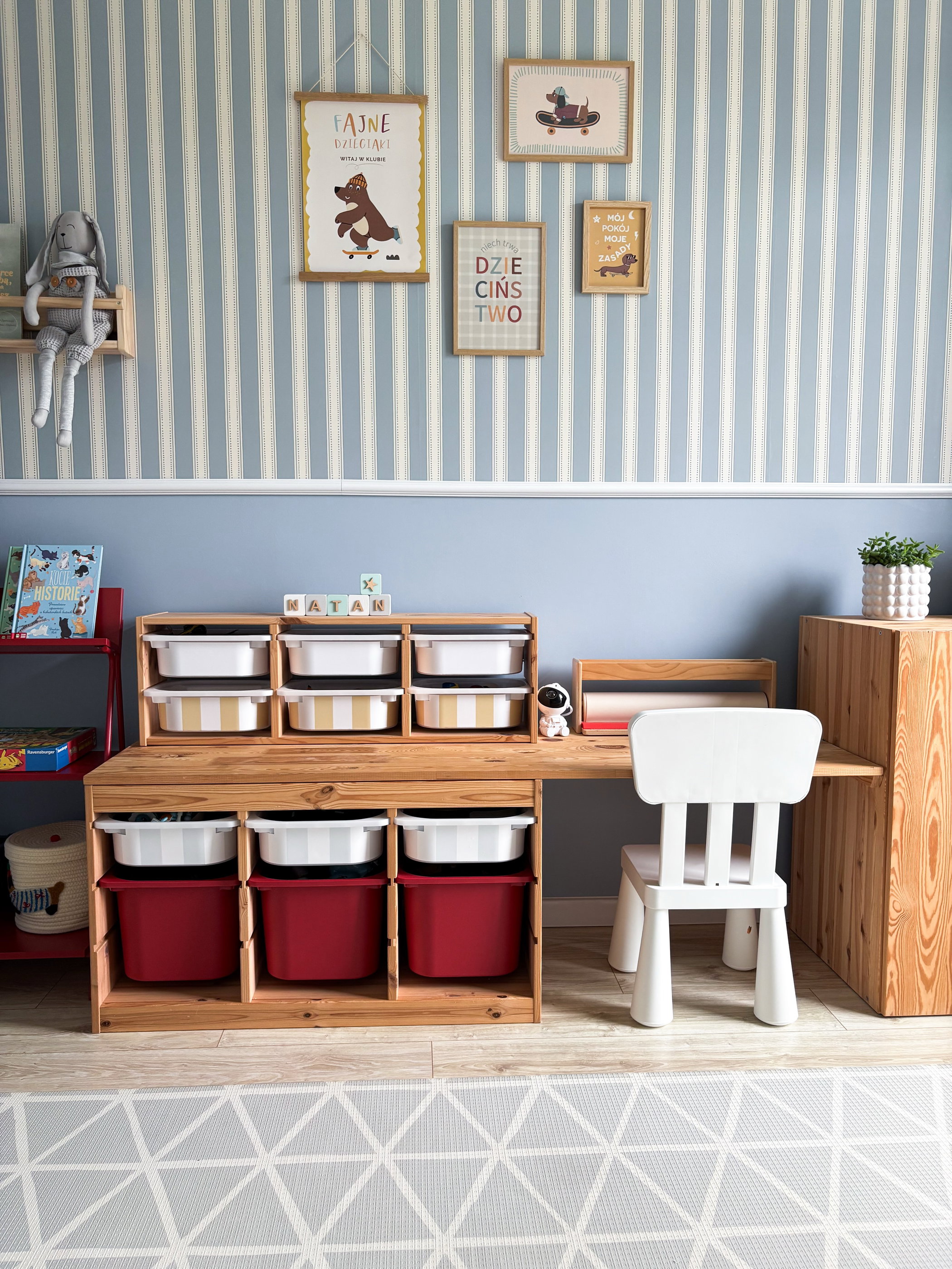 Children's room with a wooden desk, storage bins, and a white chair against a striped wall.