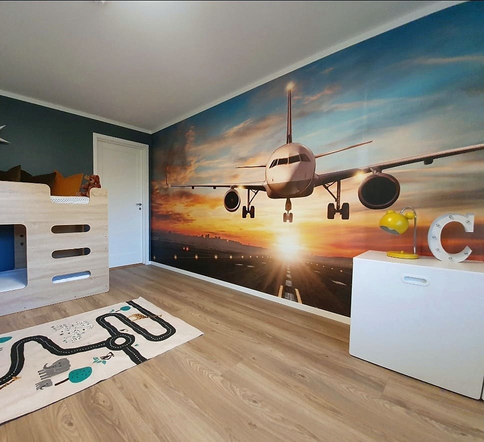 Child's bedroom with airplane mural, wooden bunk bed, road-themed rug, and white storage cabinet.