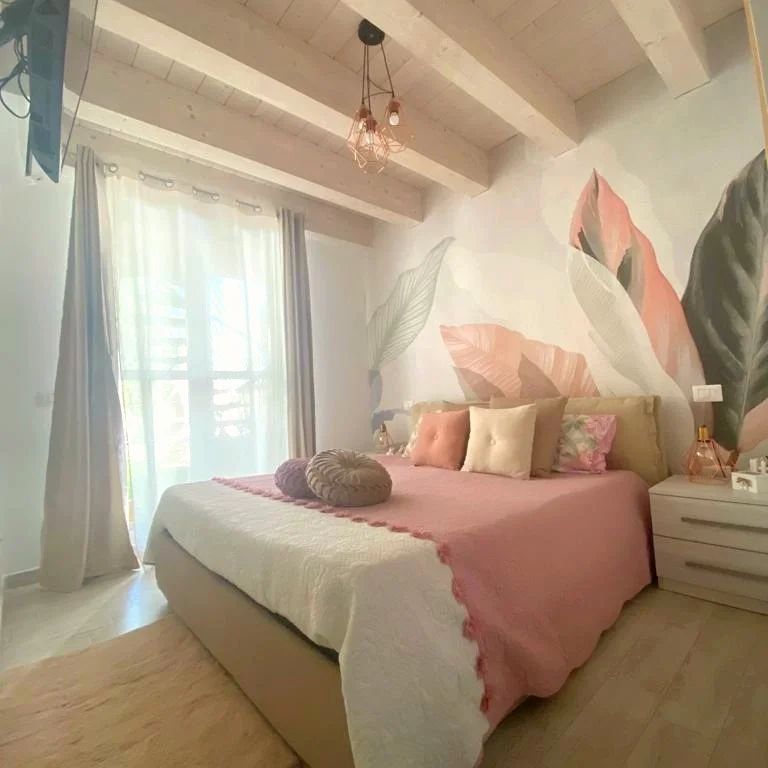 Camera da letto con biancheria da letto rosa, arte murale floreale e travi a vista.
