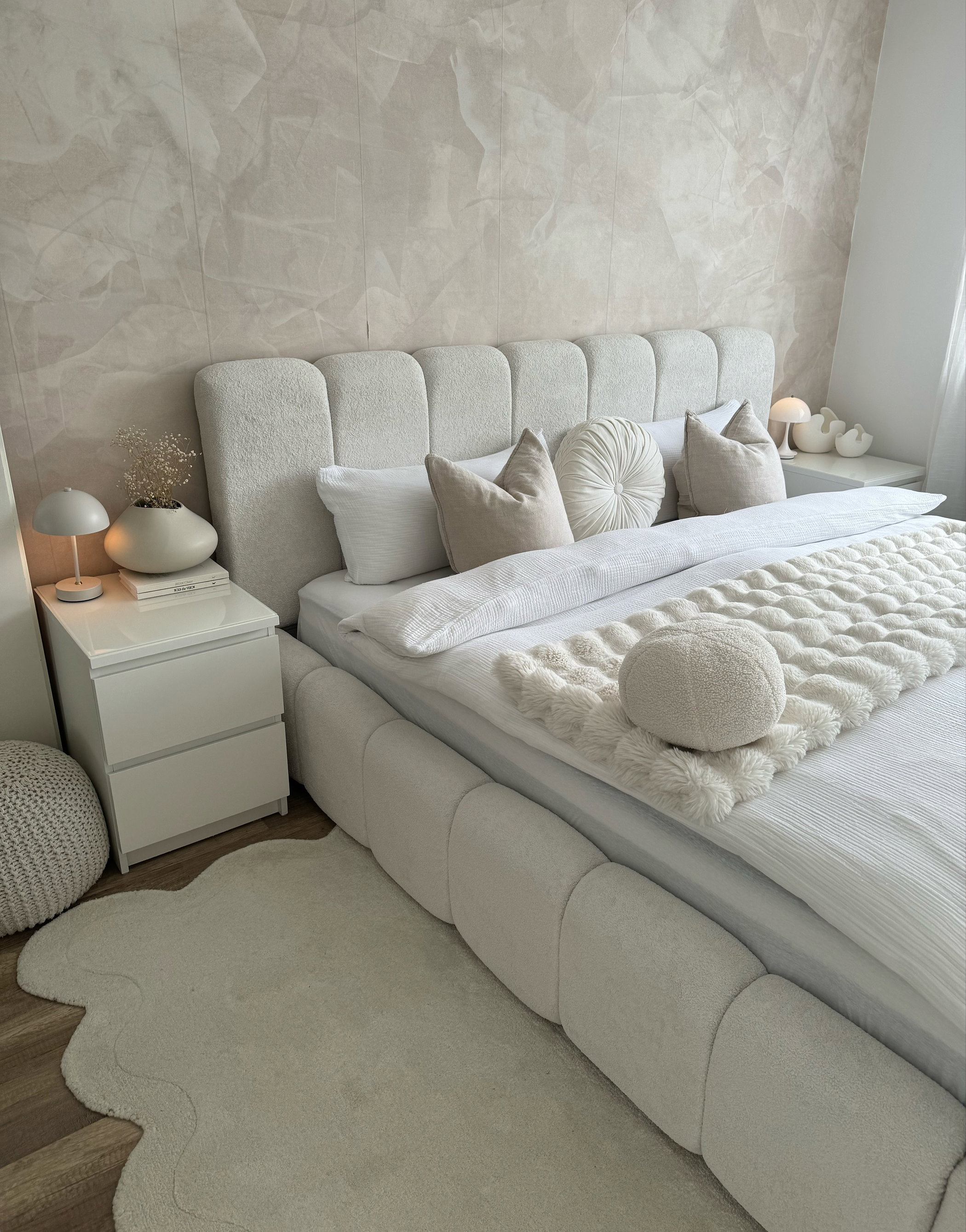 A plush white bed with textured pillows sits on a rug.