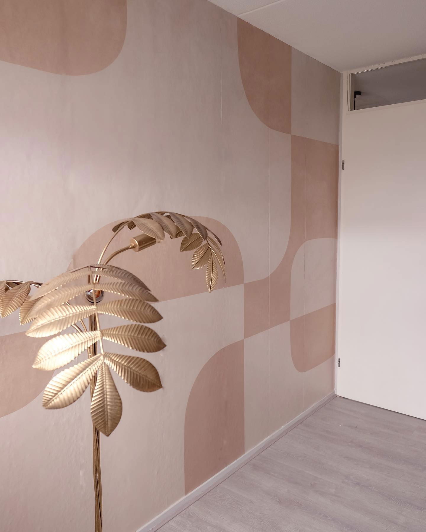 Innenraum mit Blattgoldlampe, geometrischer Tapete in Rosatönen und einer weißen Tür.