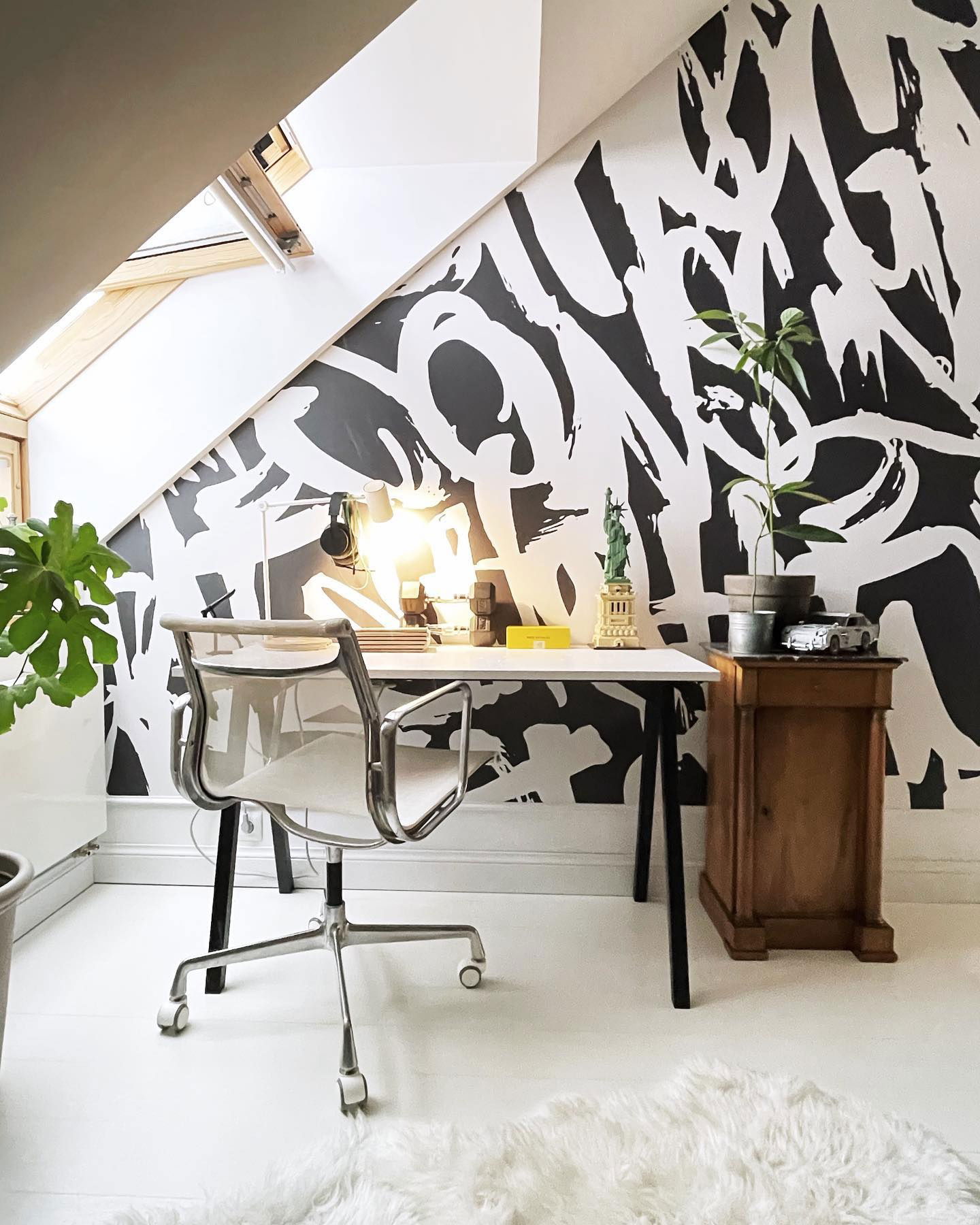Home office setup with white desk, mesh chair, and black and white graffiti-style wall art.