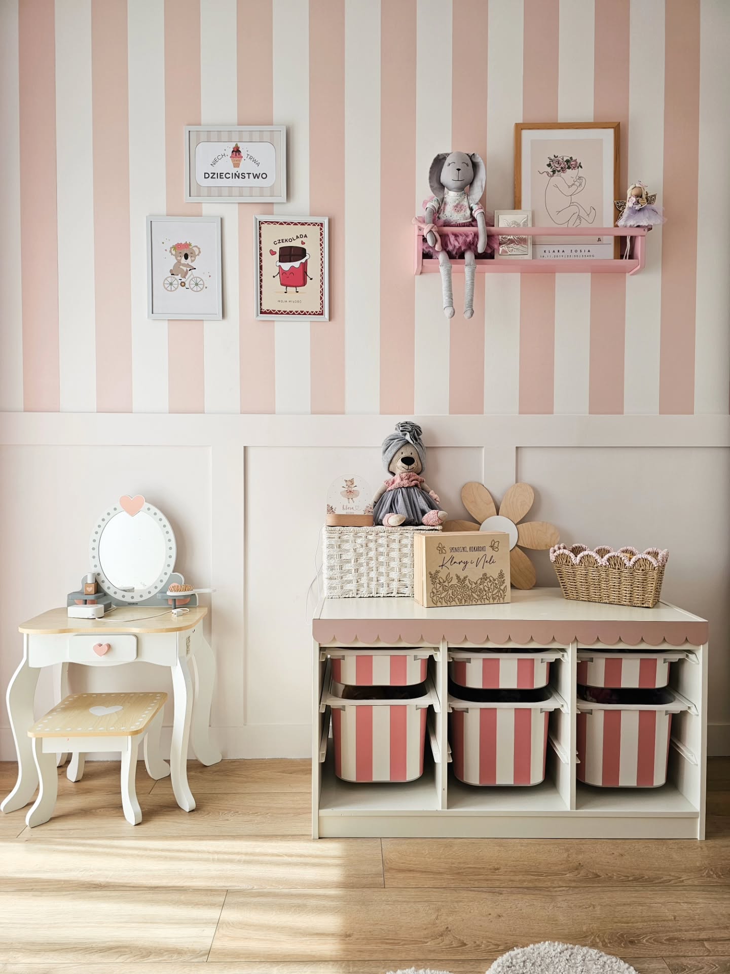 Kinderzimmer mit rosa und weiß gestreifter Tapete, einem weißen Schminktisch mit Herzspiegel und einer weißen Aufbewahrungseinheit mit rosa und weiß gestreiften Körben.