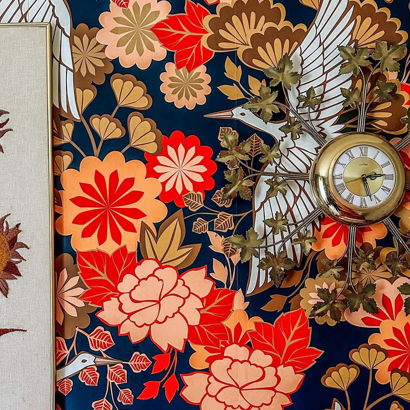 Floral wallpaper with cranes, a framed sunflower, and a gold United clock with leaf accents.