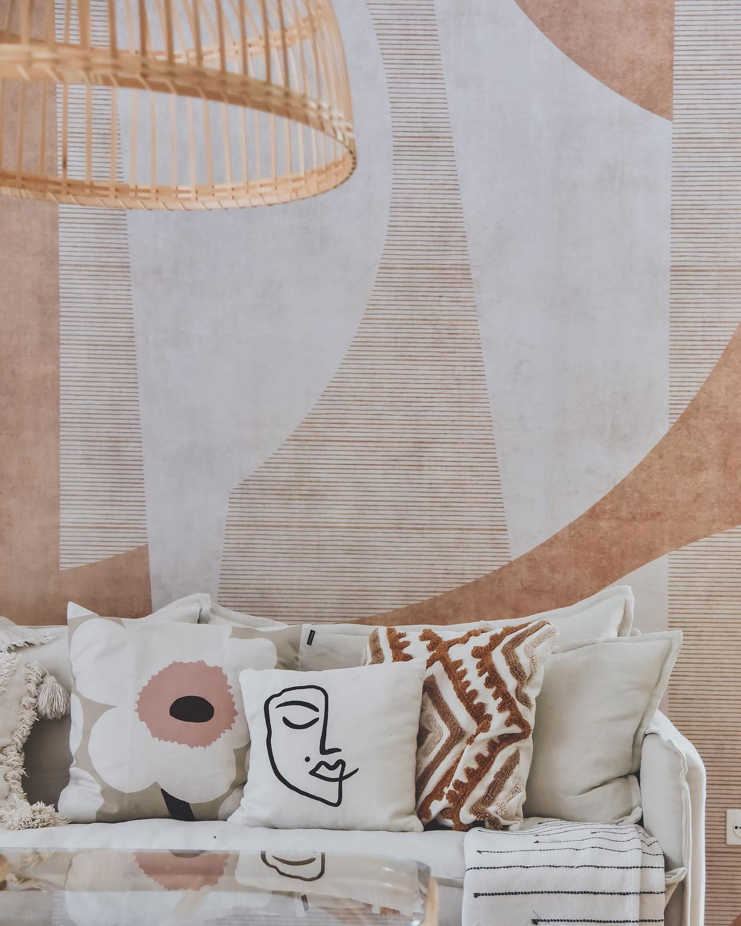 Woonkamer met witte bank, decoratieve kussens en geometrisch behang.