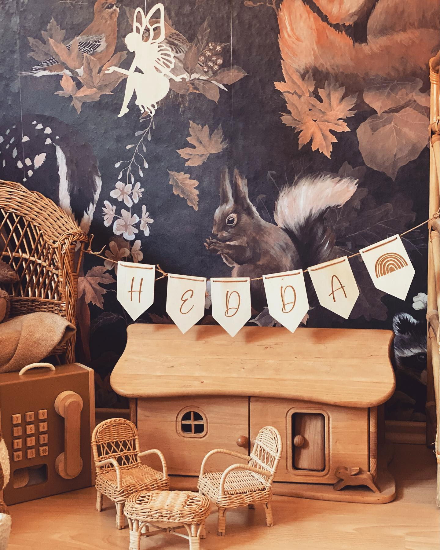 Chambre d'enfant avec papier peint sur le thème de la forêt, maison de poupée en bois et bannière "Hedda".