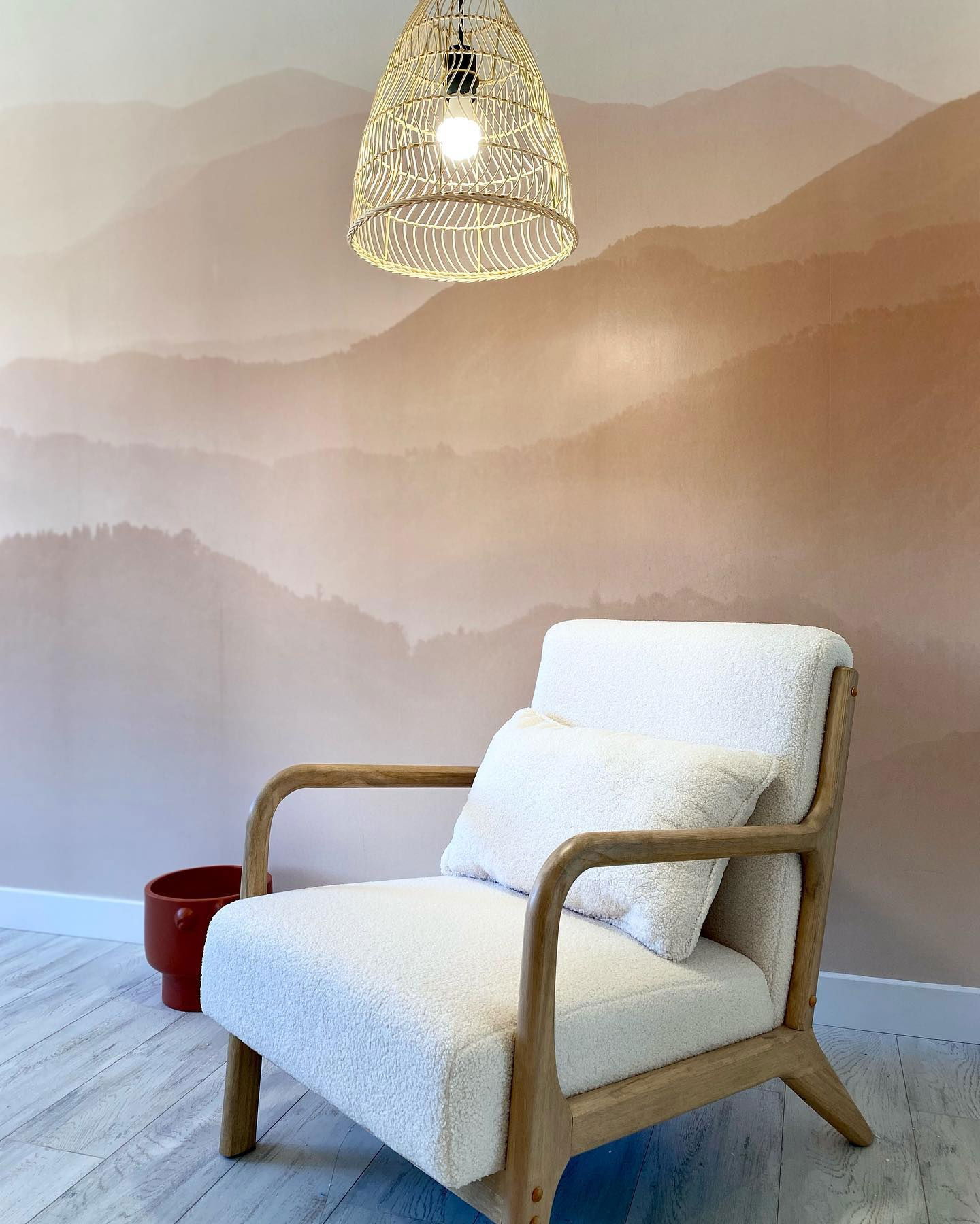 Interieur met witte sherpa stoel, bergmuurschildering en geweven hanglamp.