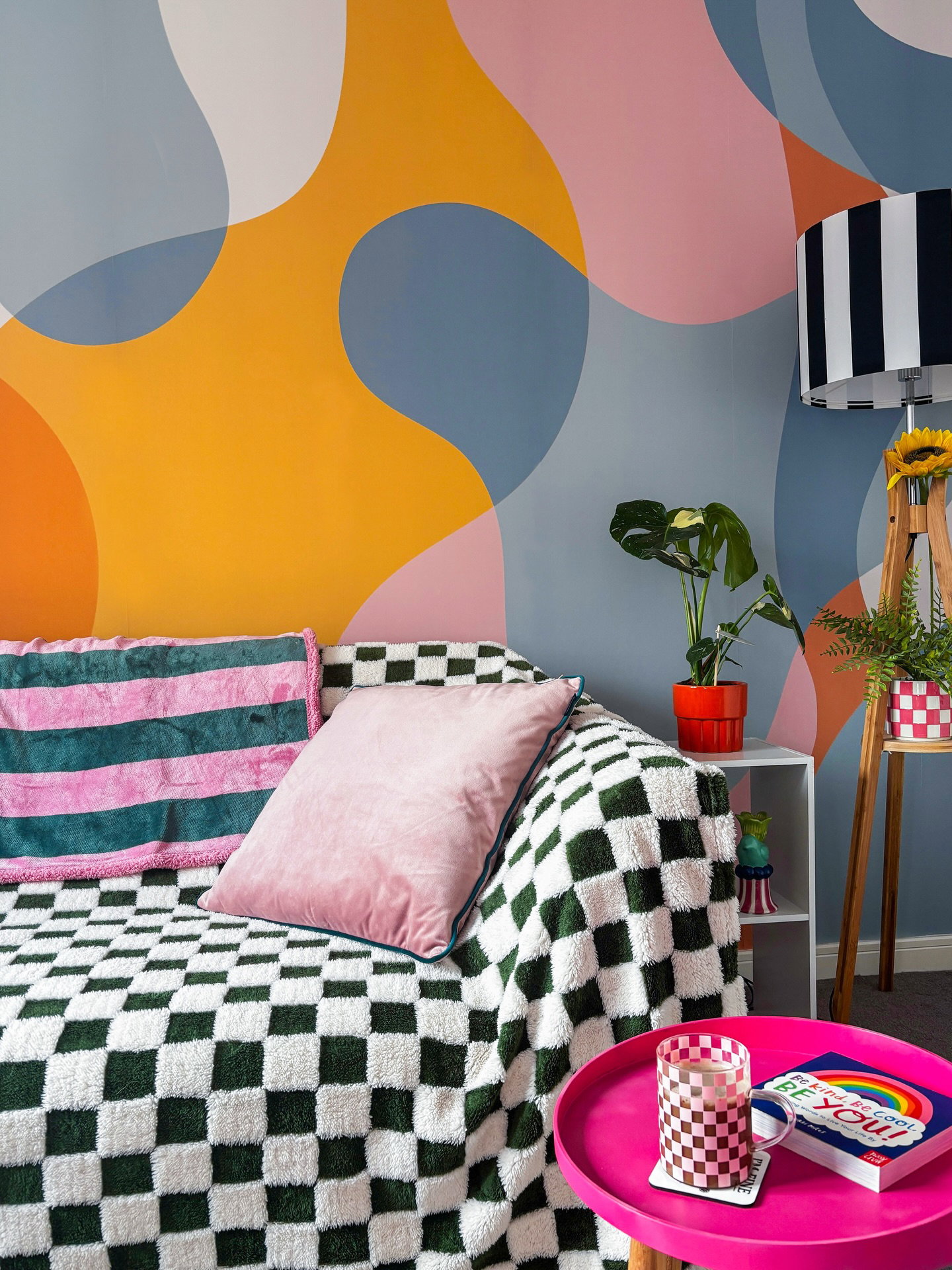 Grønt og hvitt rutete teppe dekker en sofa med rosa og stripete puter.