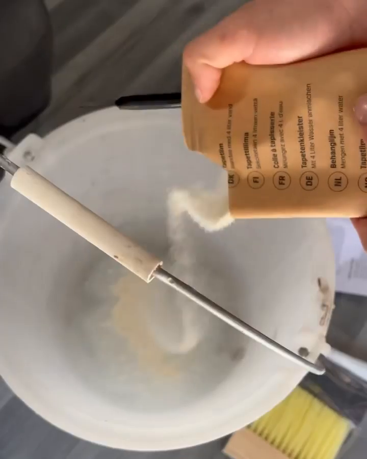 Powder being poured from a packet into a bucket of water to make wallpaper paste.
