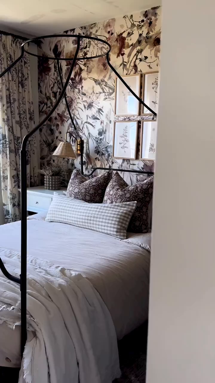 Bedroom with floral wallpaper, black canopy bed, and white bedding.