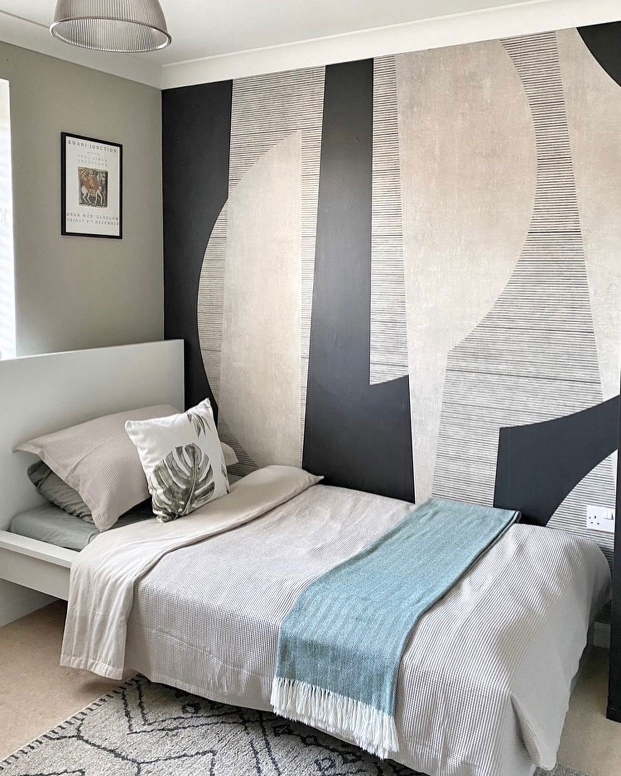 Bedroom with single bed, gray linens, blue throw, and geometric wallpaper.