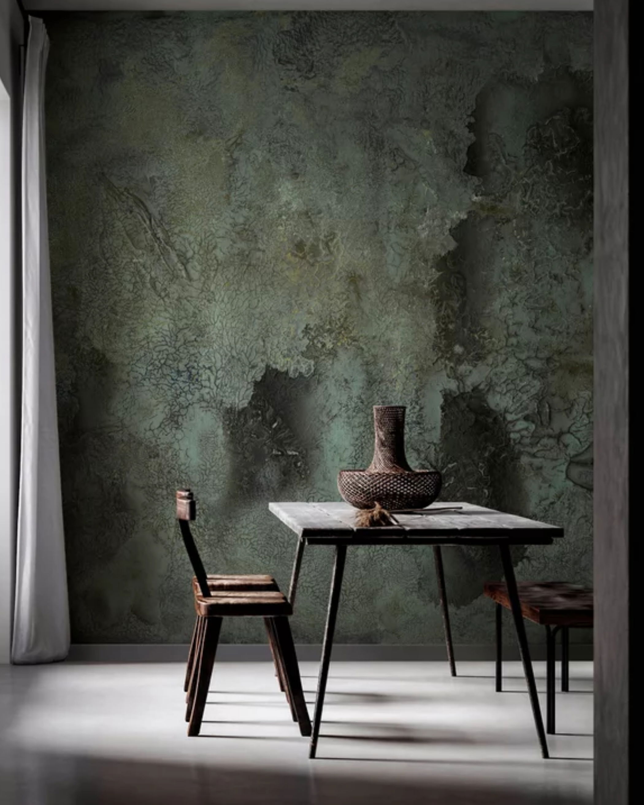 Interior with textured green wall, table, vase, and wooden chair.