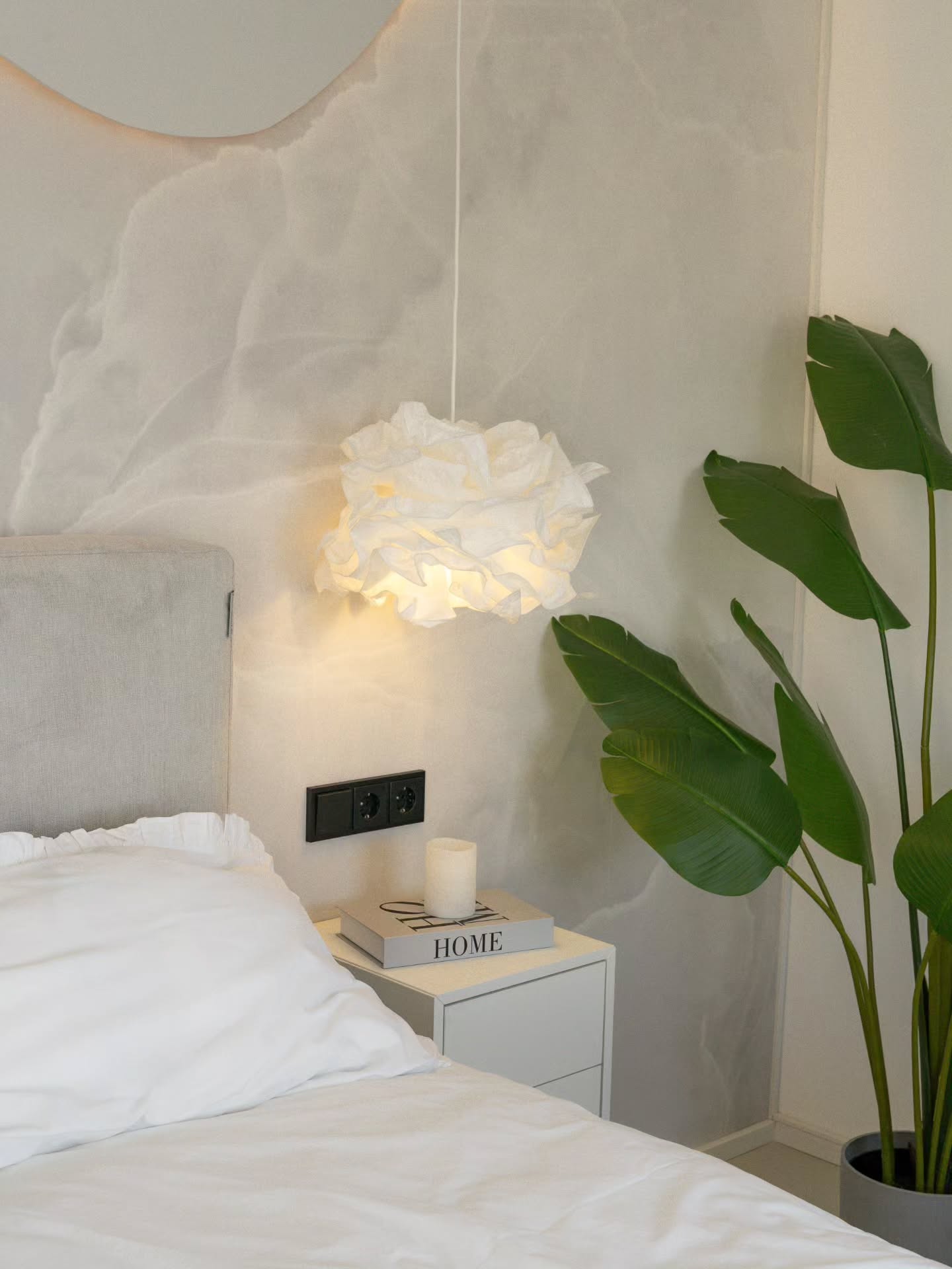 Scène de chambre avec suspension blanche, plante et table de chevet.