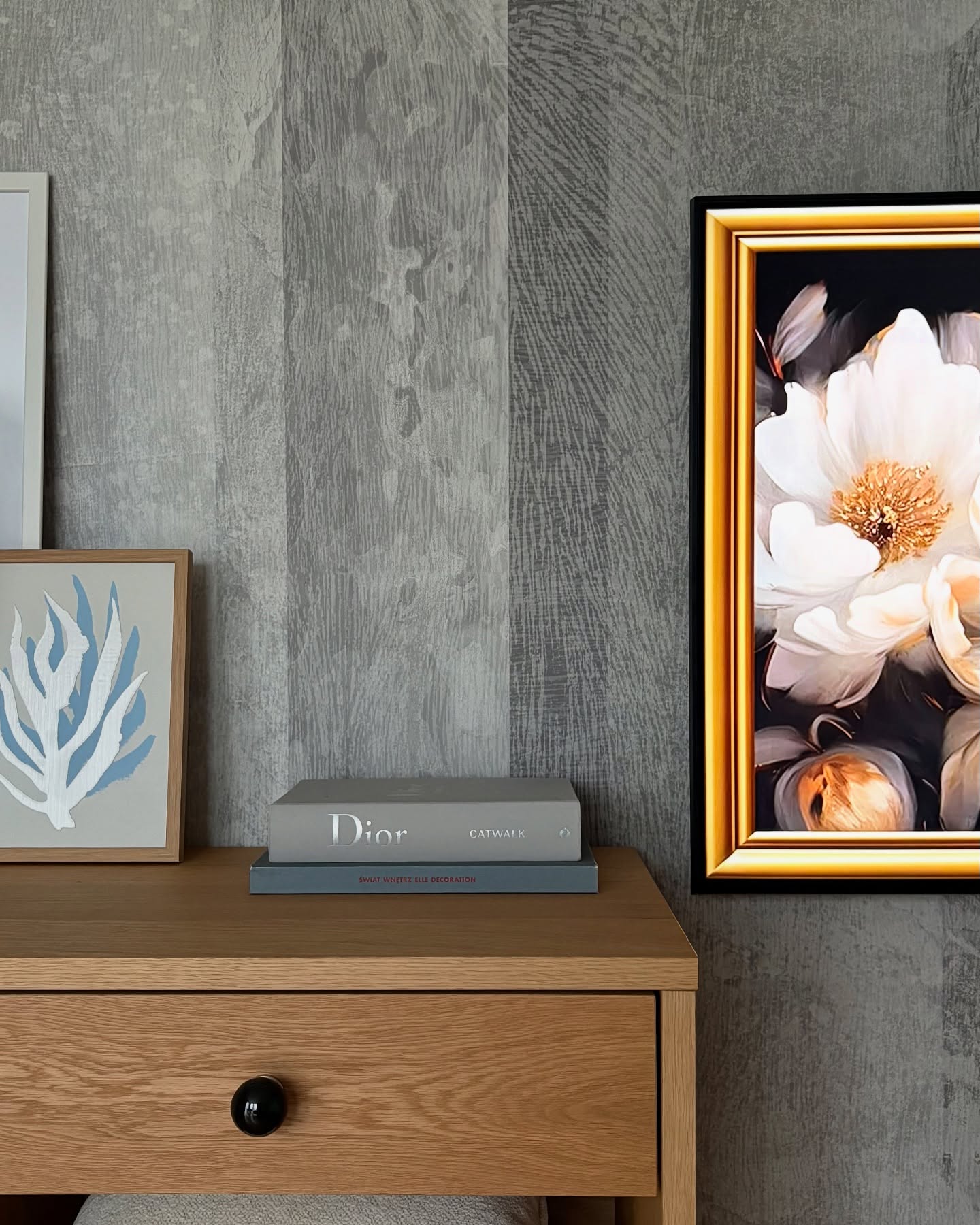 Interior with wood-look wallpaper, floral art, and a wood nightstand with Dior books.