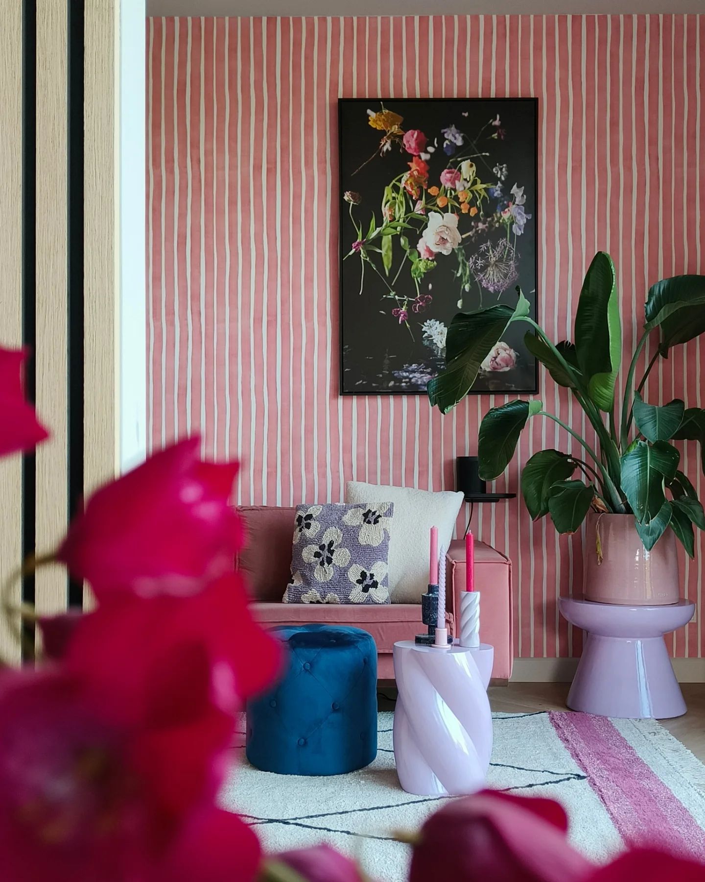 Living room with pink striped wallpaper, floral art, pink sofa, and blue ottoman.