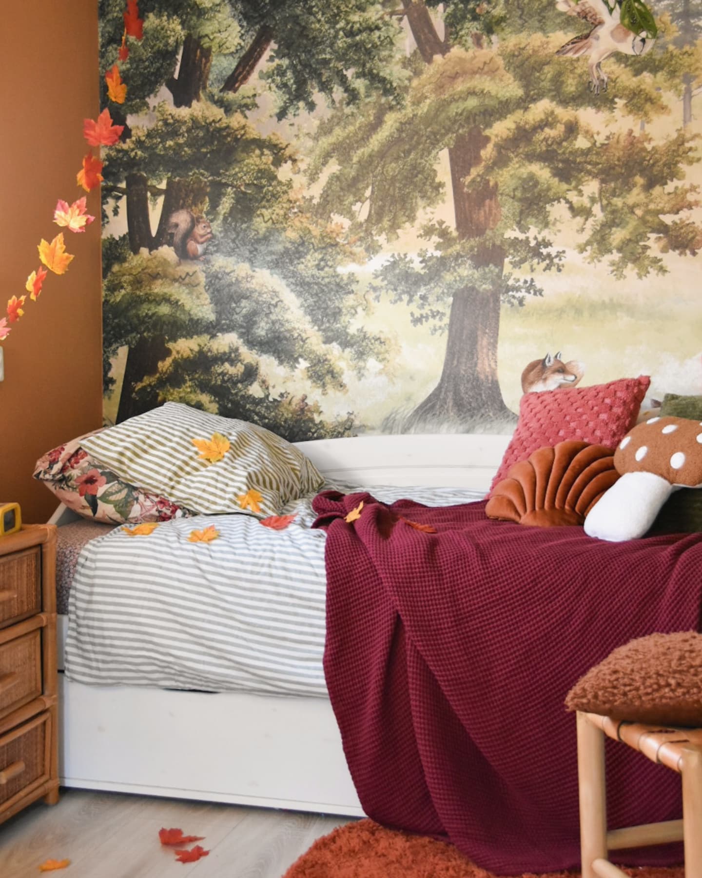 Child's room with forest mural, white daybed, and fall decor.