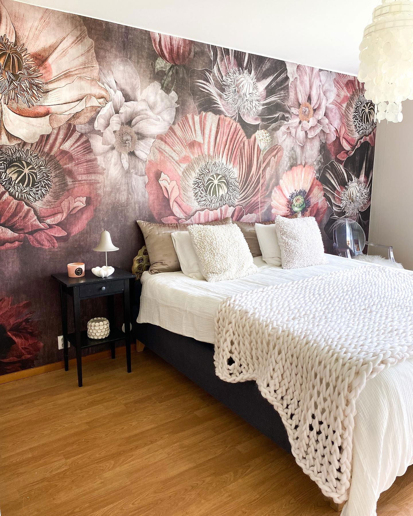 Slaapkamer met bloemenbehang, wit beddengoed en grof gebreide sprei.
