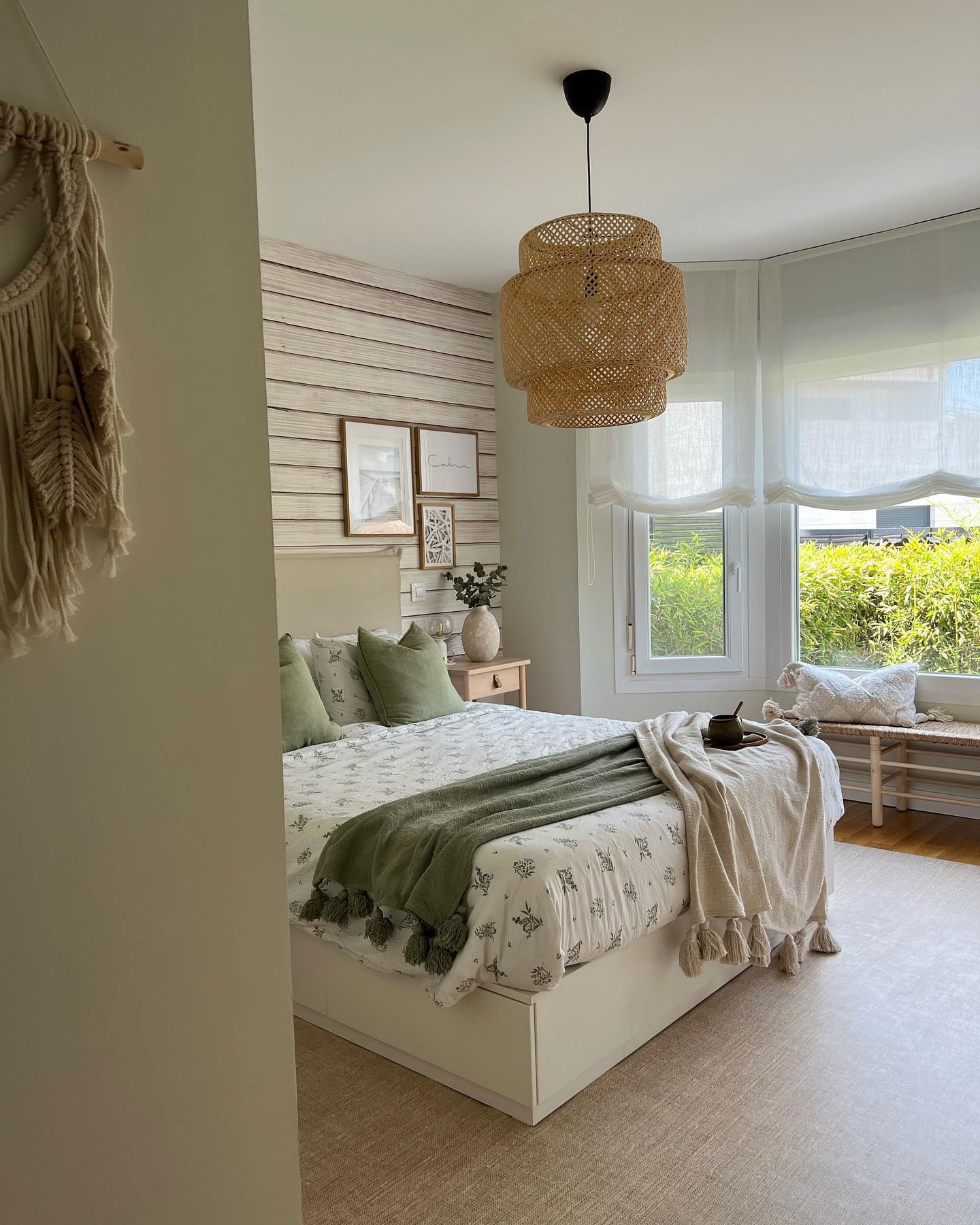 Cozy bedroom with a bed, green pillows and throw, woven light fixture, and sheer curtains.