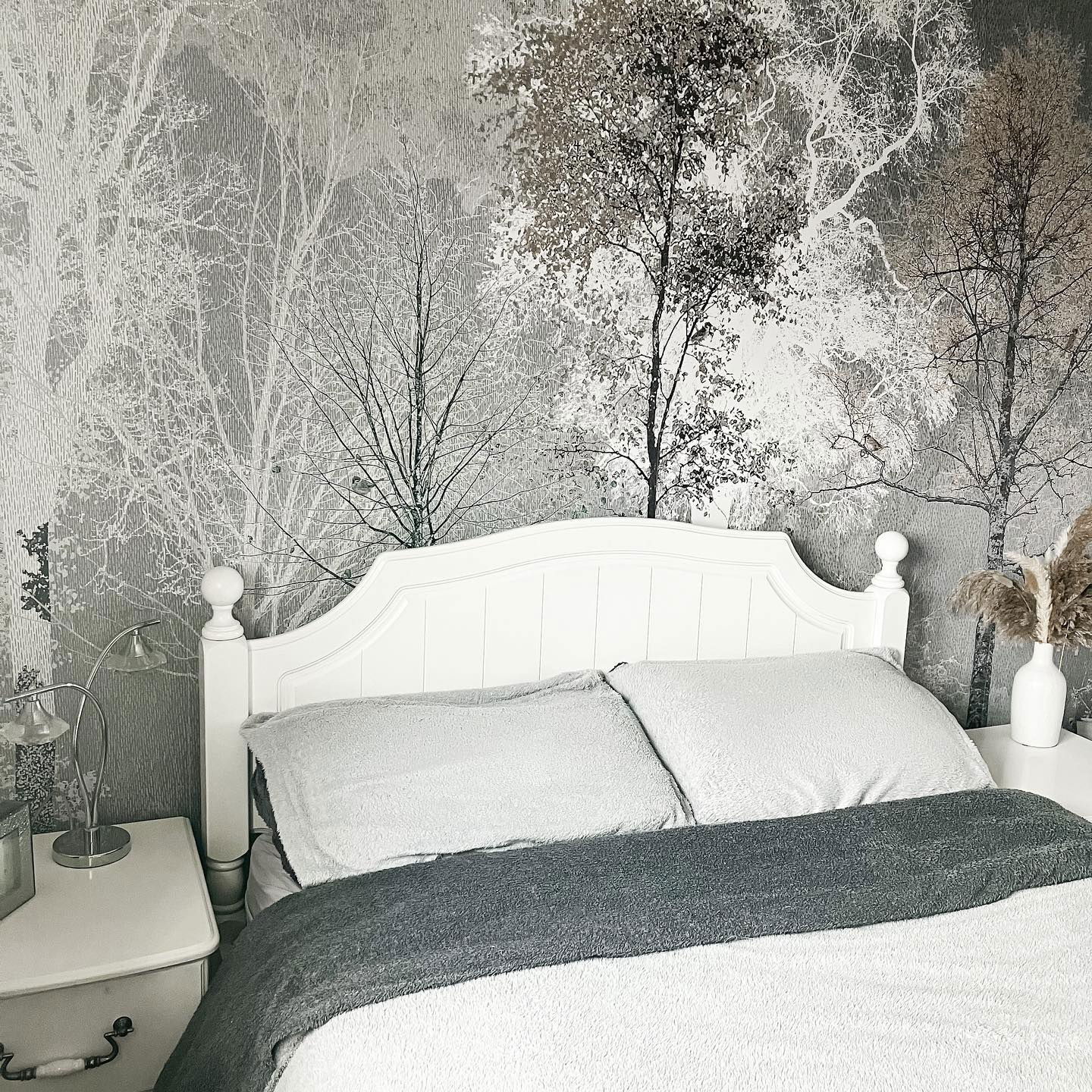 Bedroom with white bed, gray blanket, and forest-themed wallpaper.