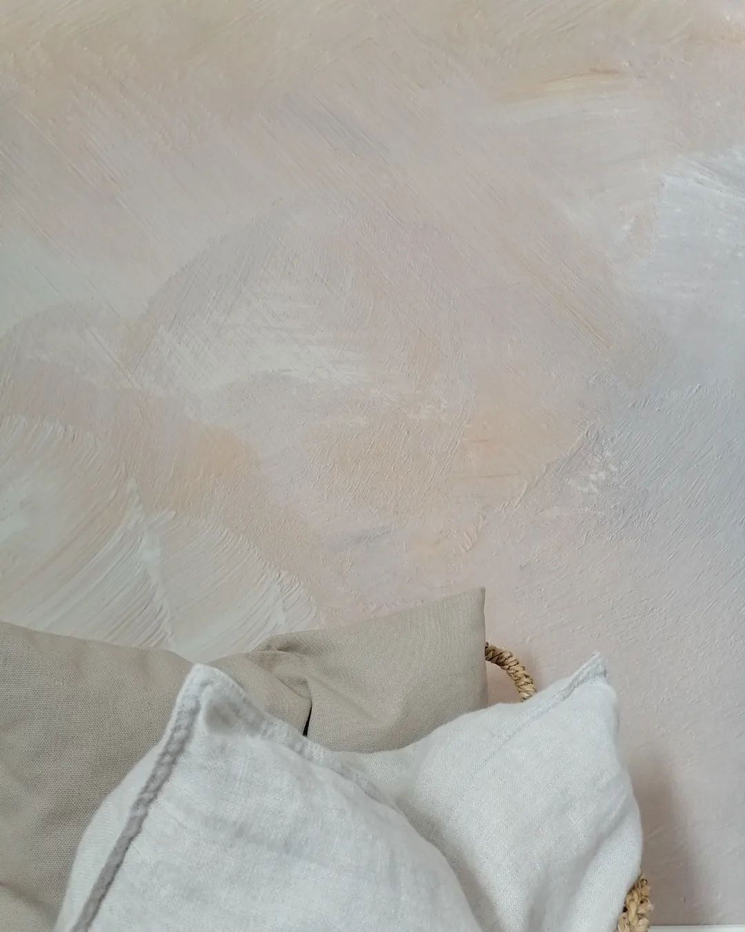 Neutral linen pillows in a woven basket against a textured wall.