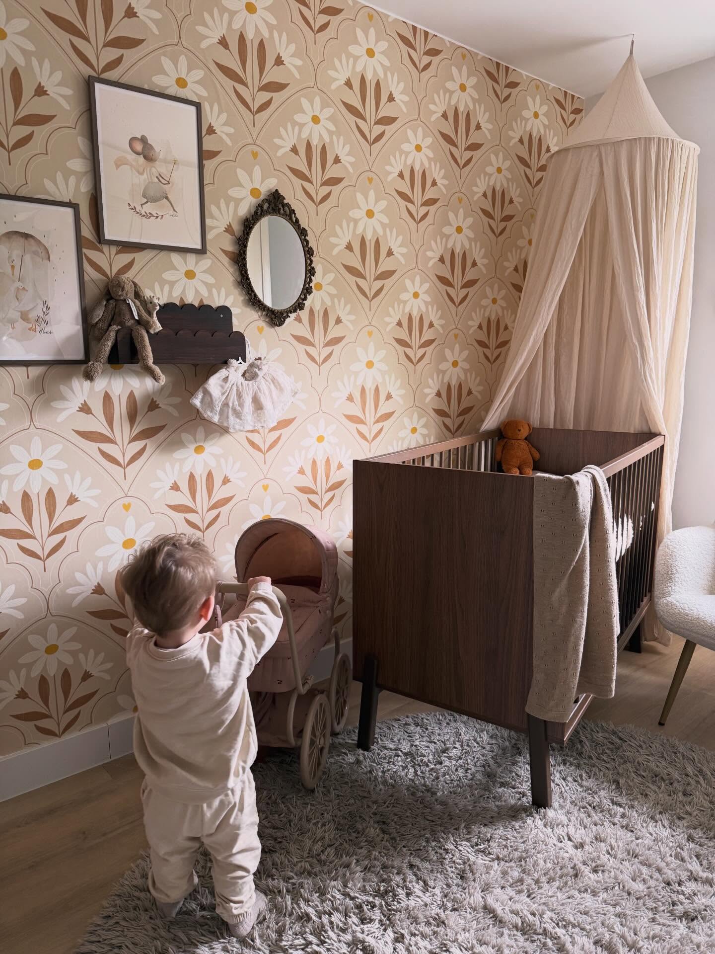 Toddler plays with a doll stroller in a nursery with floral wallpaper, a crib, and a canopy.