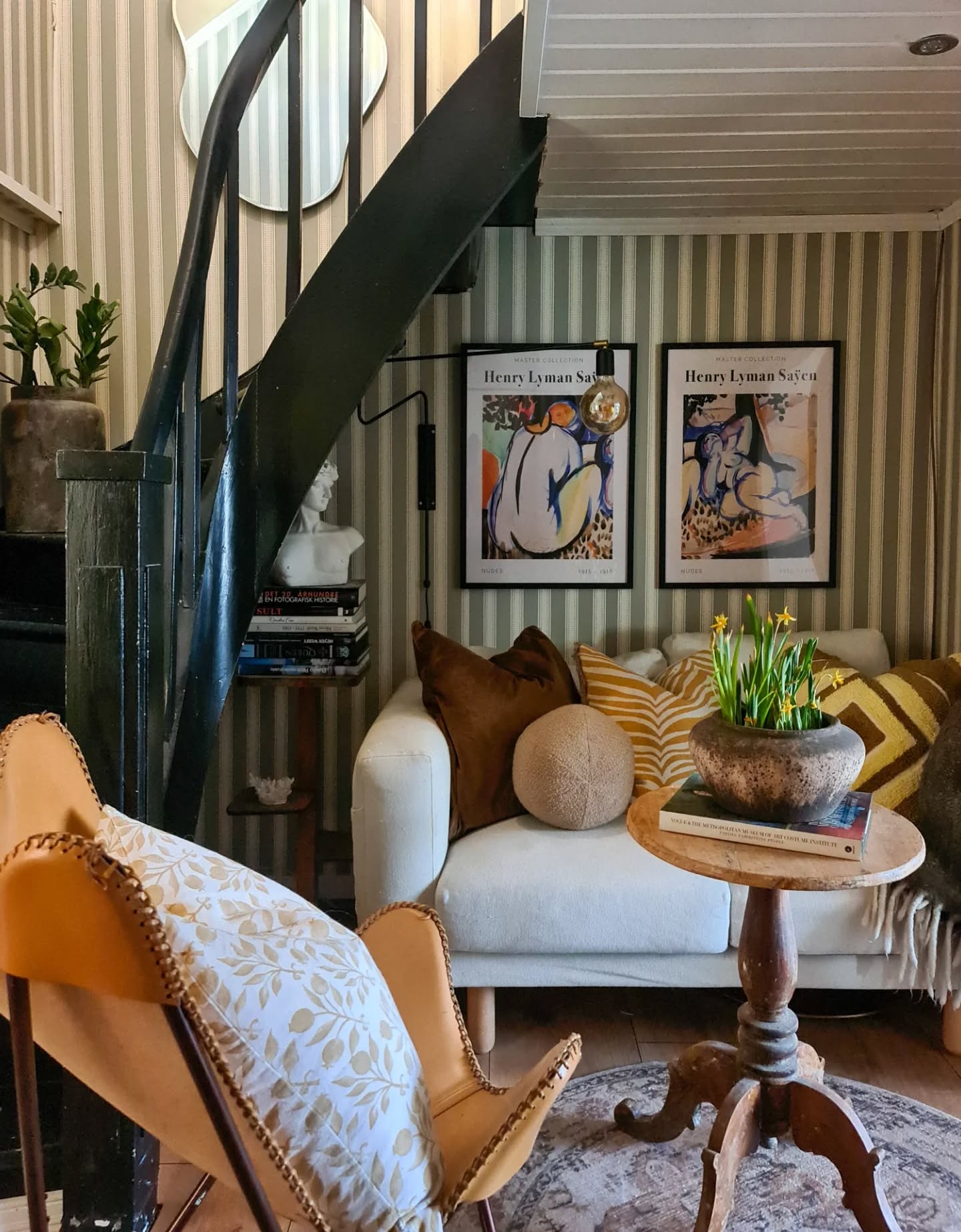 Living room with striped wallpaper, a winding staircase, butterfly chair, and sofa with Matisse prints.