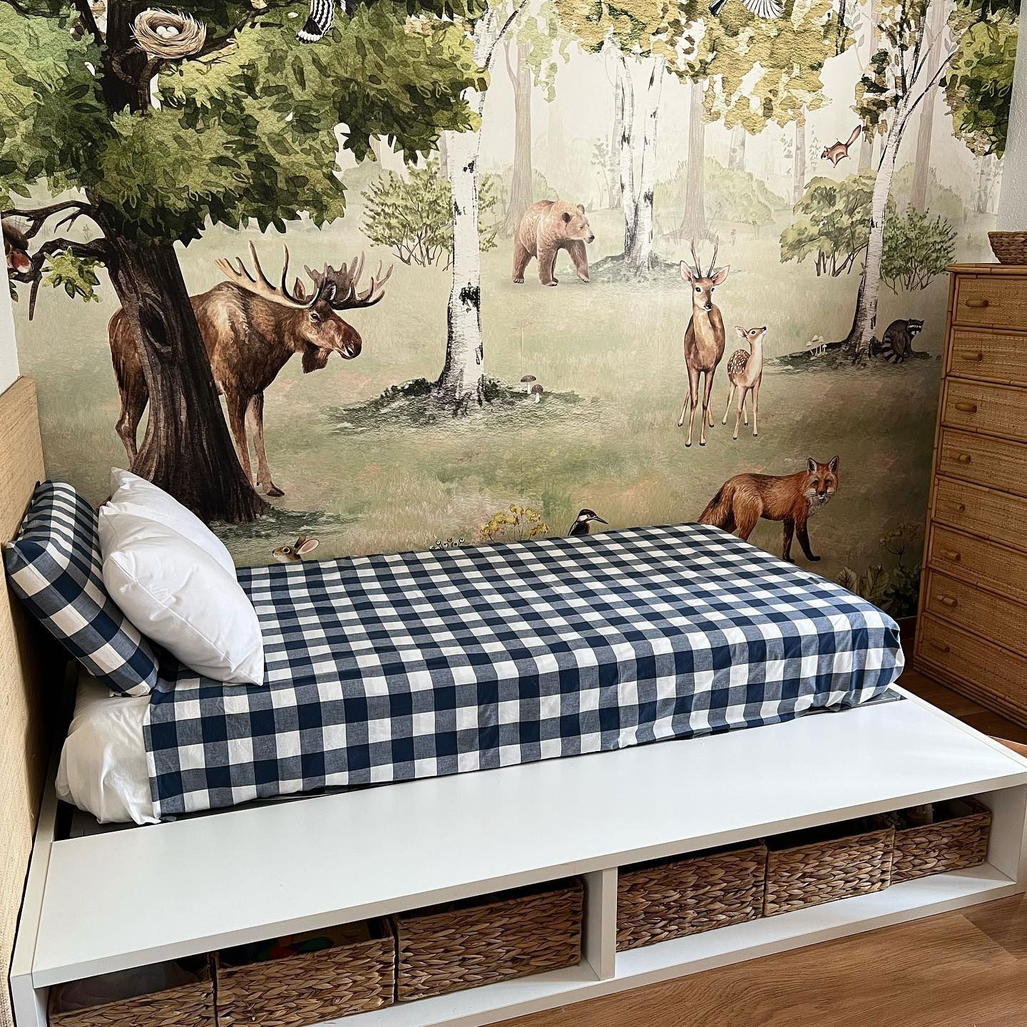 Stanza per bambini con letto bianco, biancheria da letto a quadretti blu e carta da parati con animali del bosco.