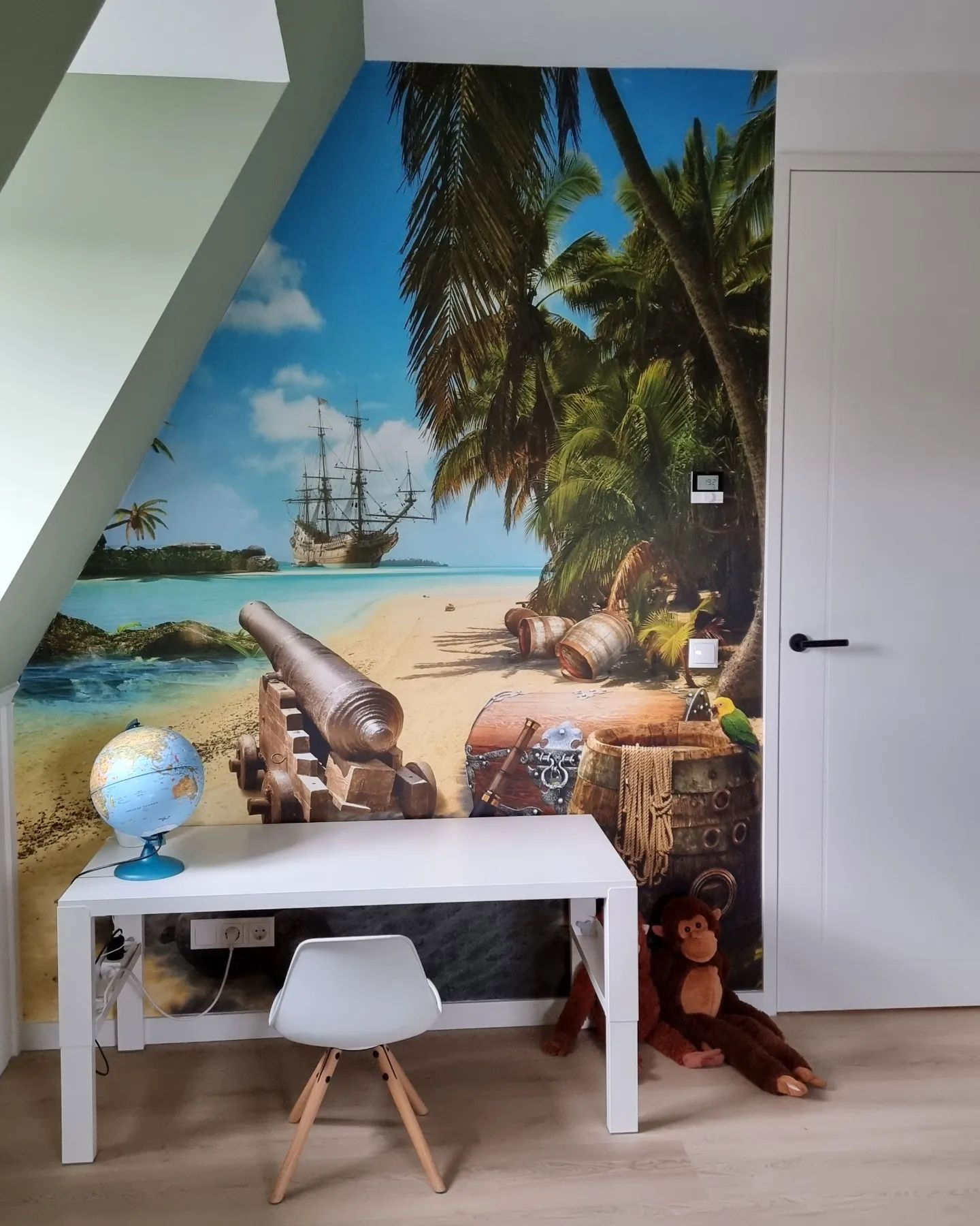 Kinderzimmer mit Piratenwandbild, weißem Schreibtisch, Globus und Stoffaffe.