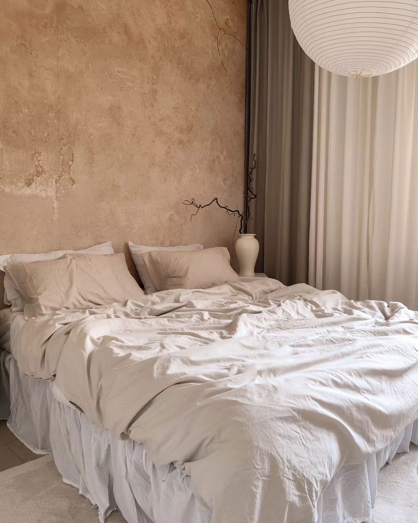 Bedroom with beige linen bedding, textured wall, and white pendant light.