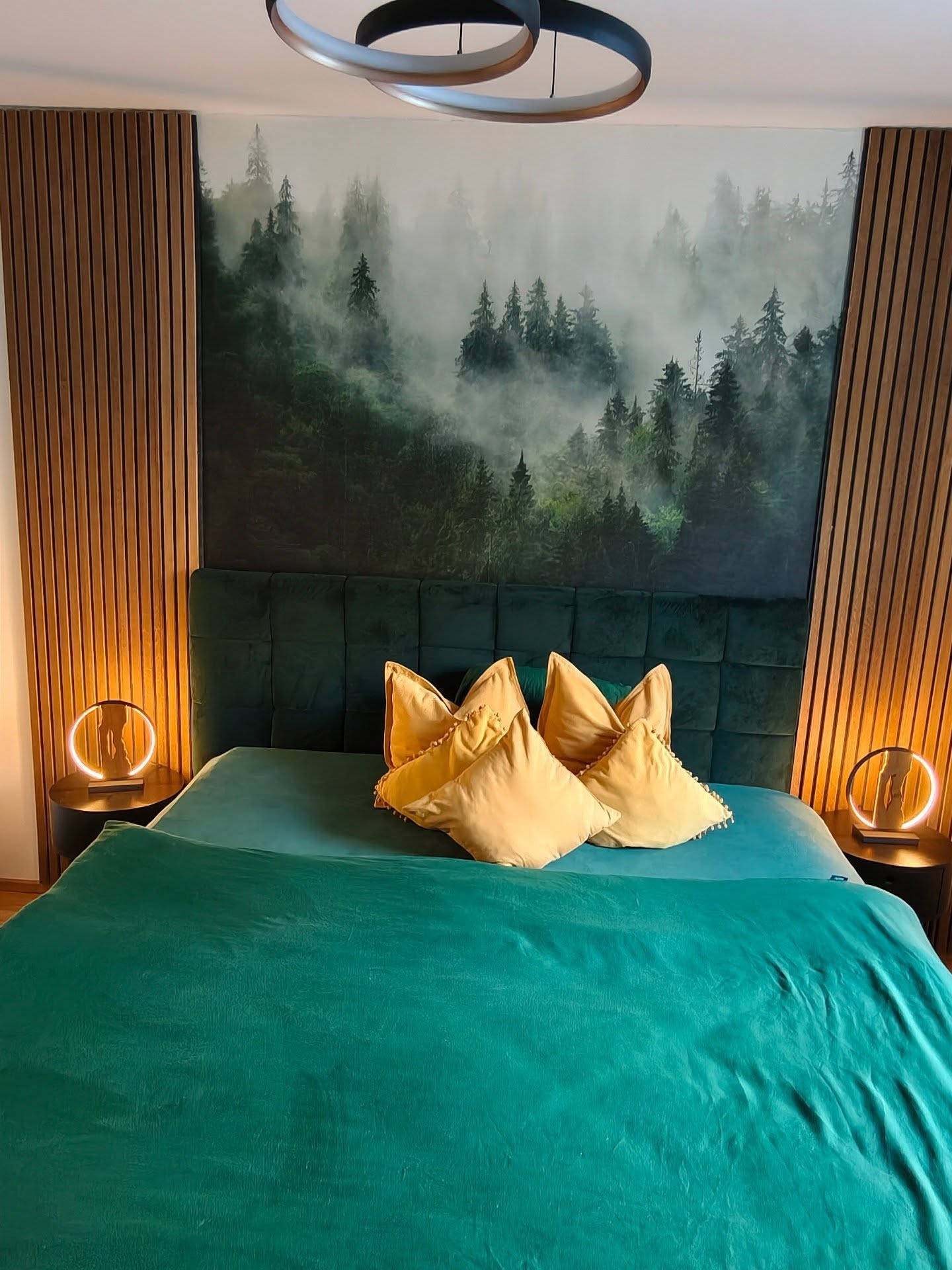 Schlafzimmer mit Wandgemälde eines Waldes, türkisfarbener Bettwäsche und gelben Kissen.