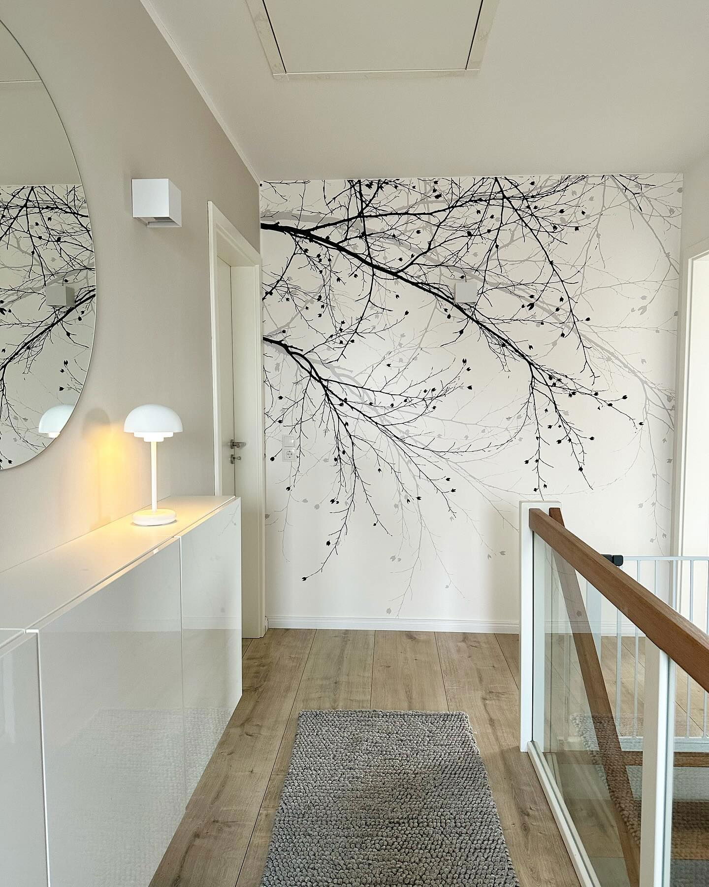 Hallway with tree branch wallpaper, wood floors, and gray rug.